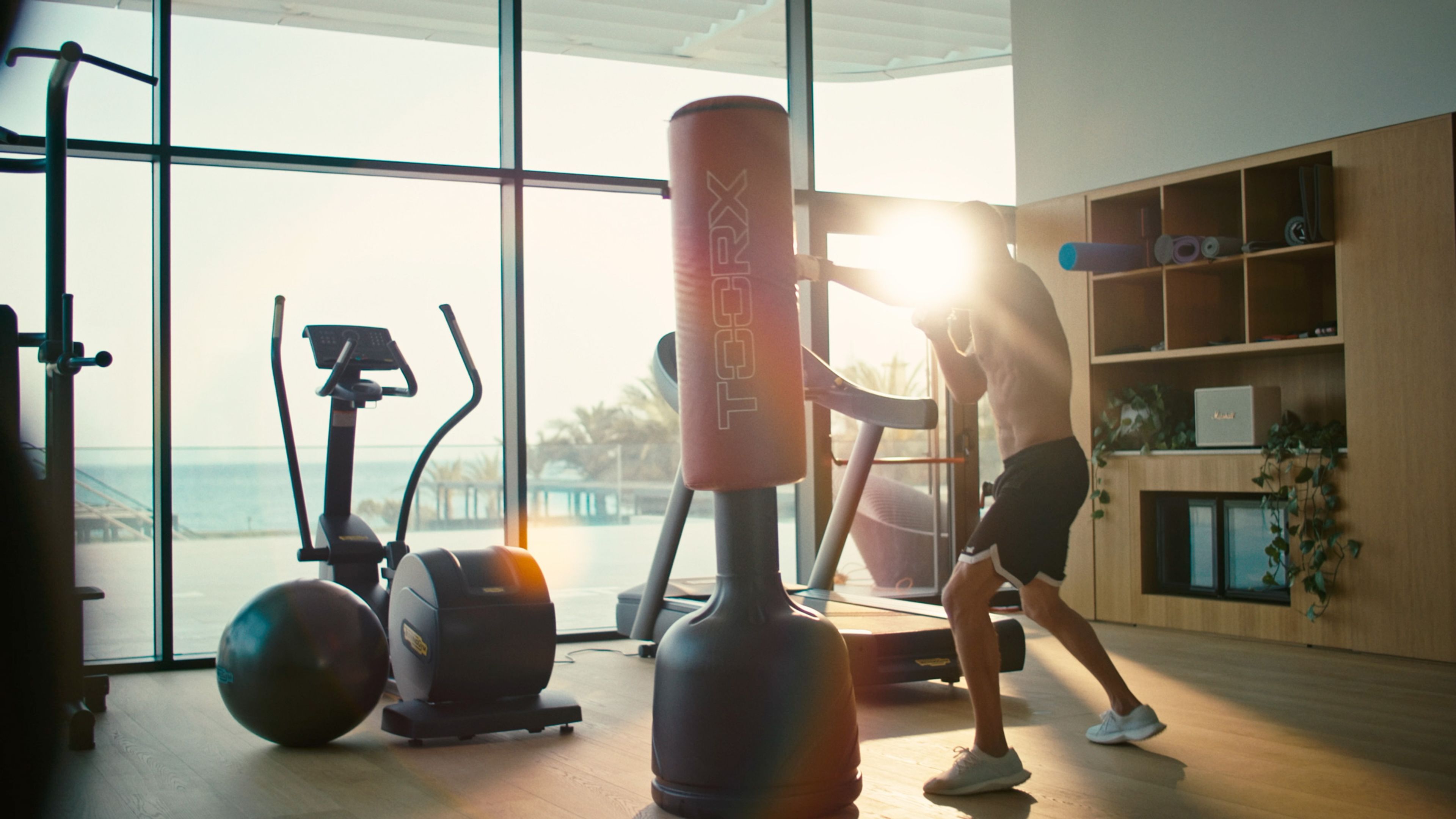 Man training with a punching bag in a gym overlooking the sea