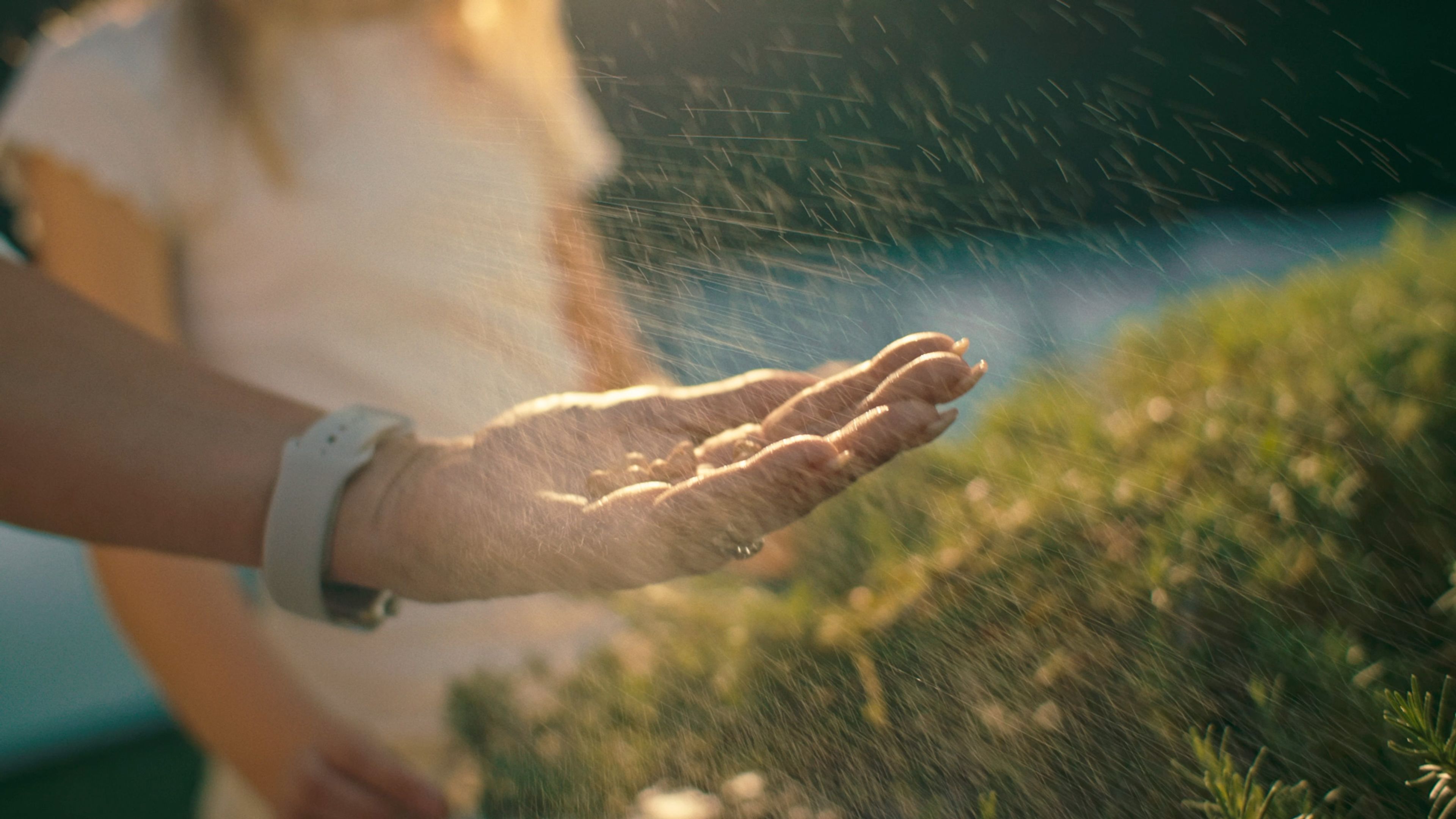 Woman holding her hand under a fine garden spray in warm sunlight