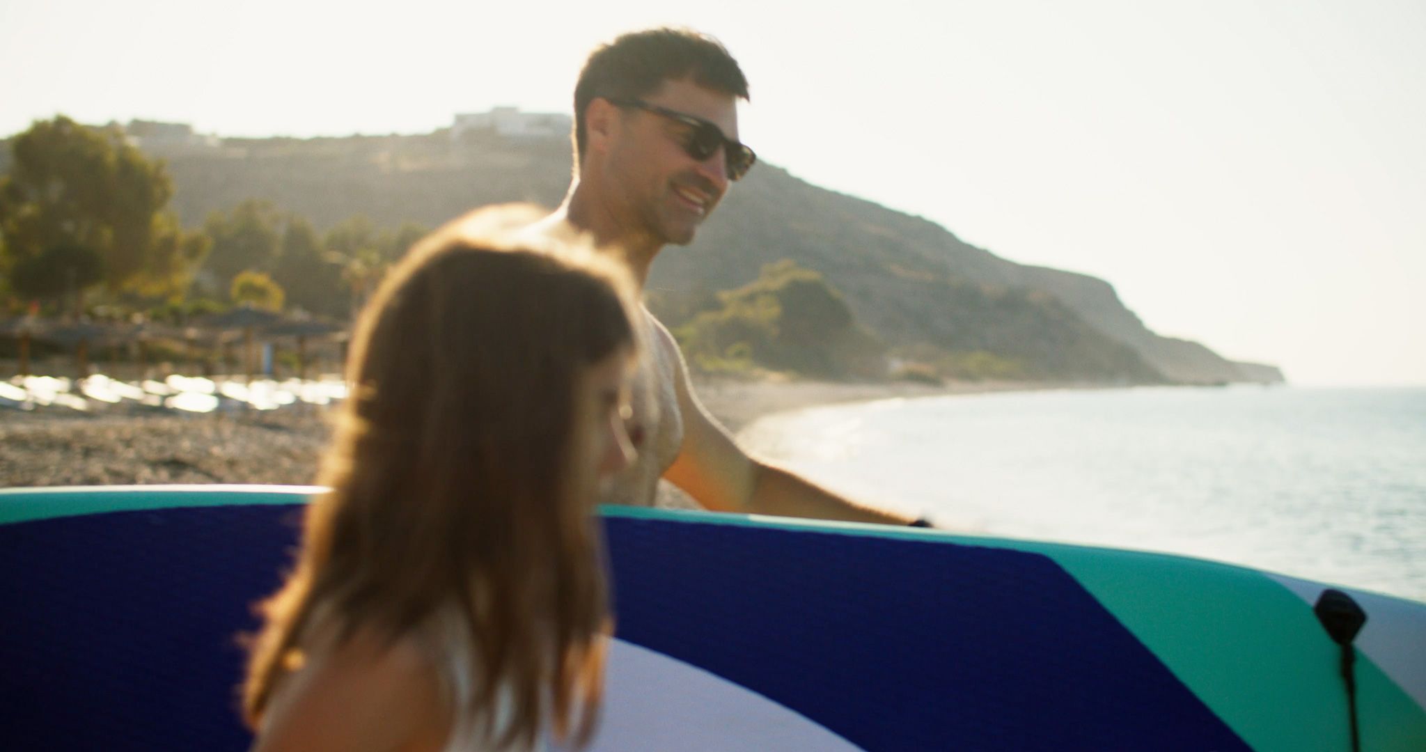 A young couple carrying a paddleboard along a quiet beach in Paphos.