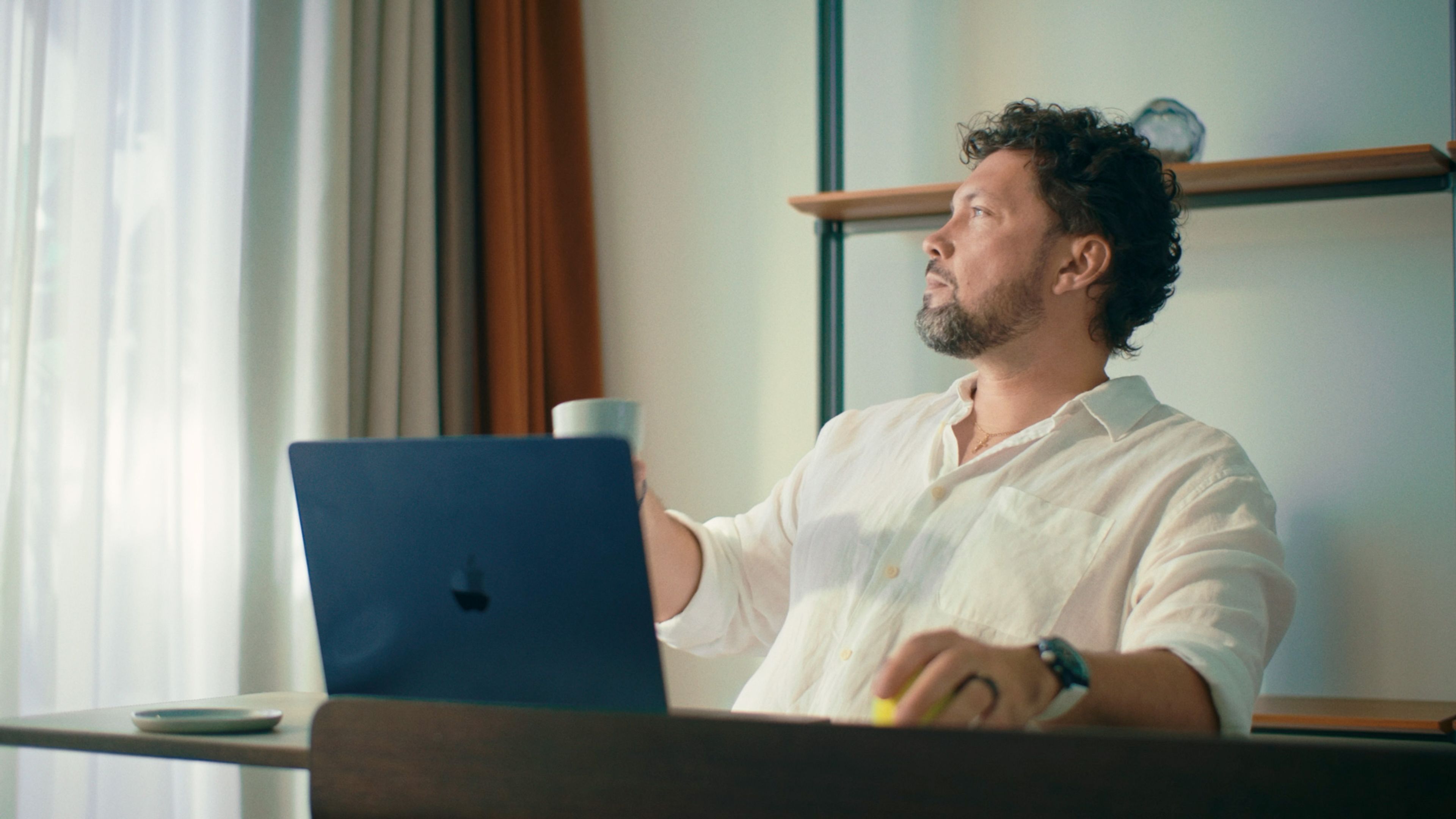 Man with a laptop and coffee sitting beside a bright window