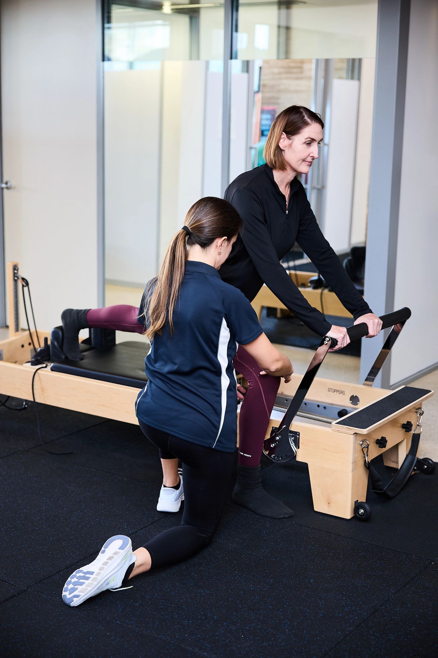 Client kneeling on a Pilates reformer as a physiotherapist guides the exercise