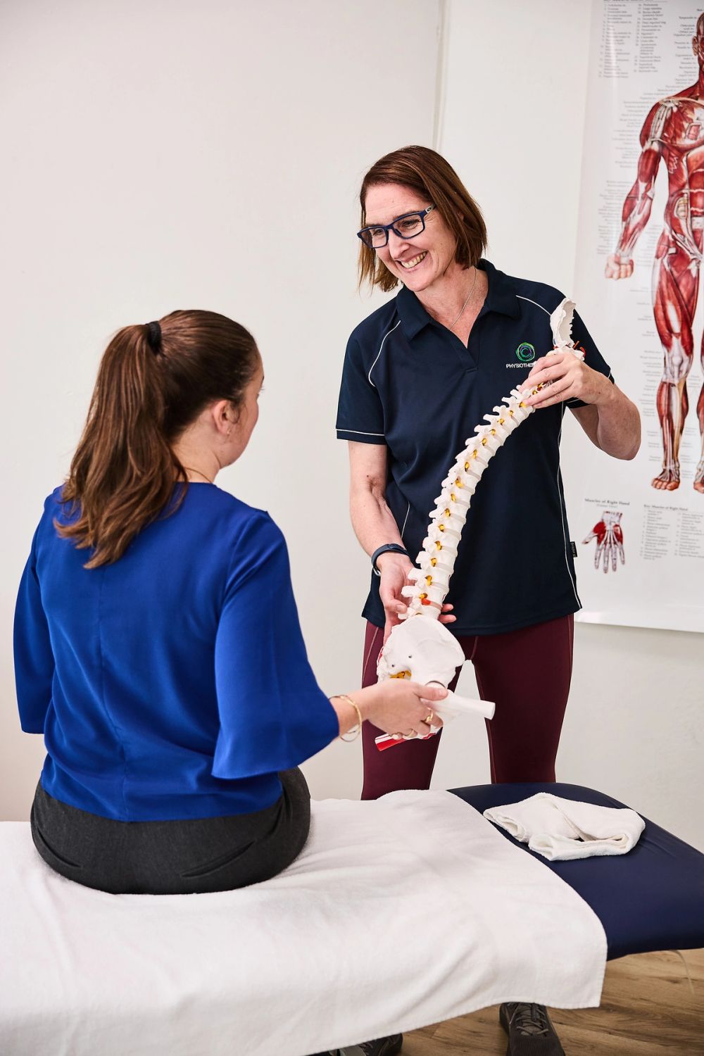 Physiotherapist using a spine model to explain a back problem to a seated patient