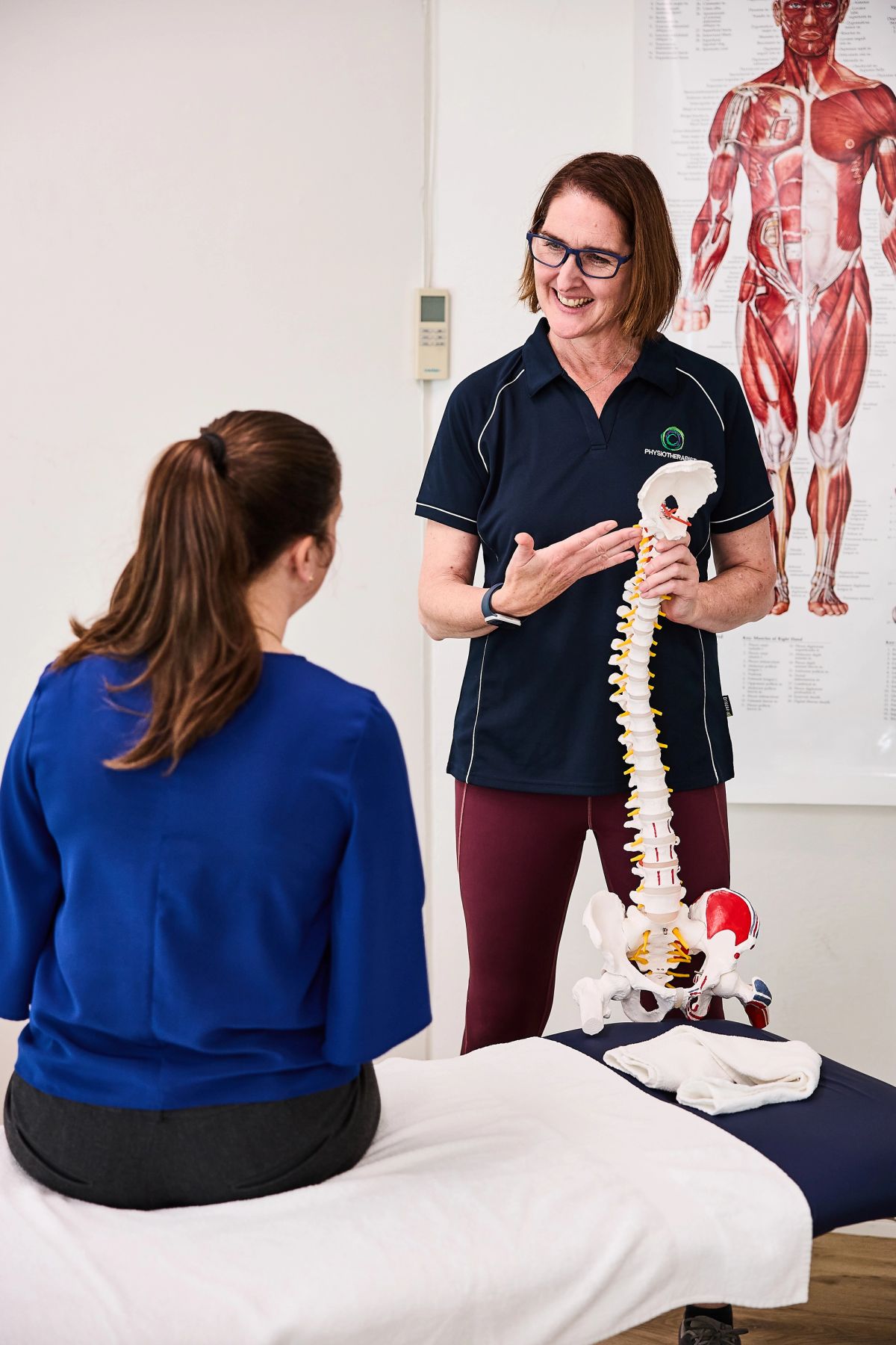 Physiotherapist using a spine model to explain a back problem to a seated patient