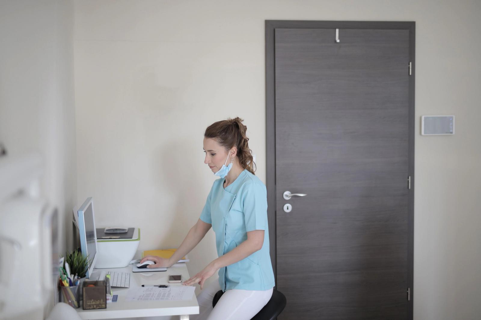 Healthcare professional wearing a mask working at a desktop computer in a modern clinic