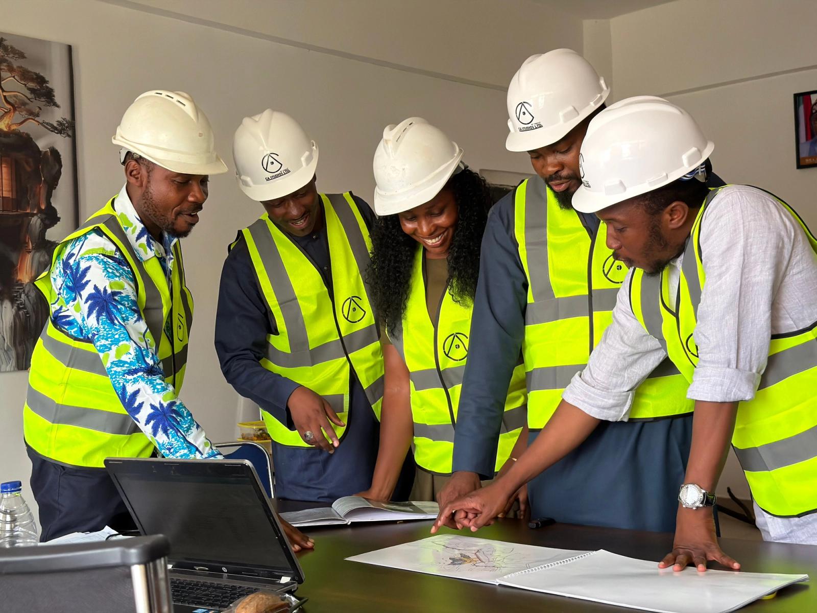 Team in hard hats and safety vests reviews work plans together in an office