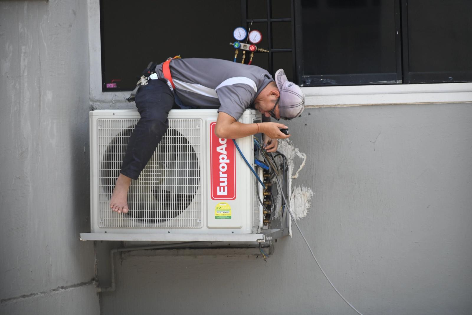 HVAC technician repairing an outdoor air-conditioning unit mounted on a building wall
