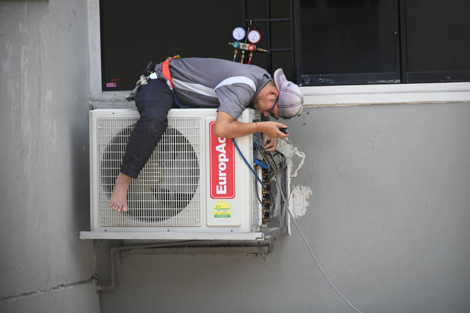 HVAC technician repairing an outdoor air-conditioning unit mounted on a building wall