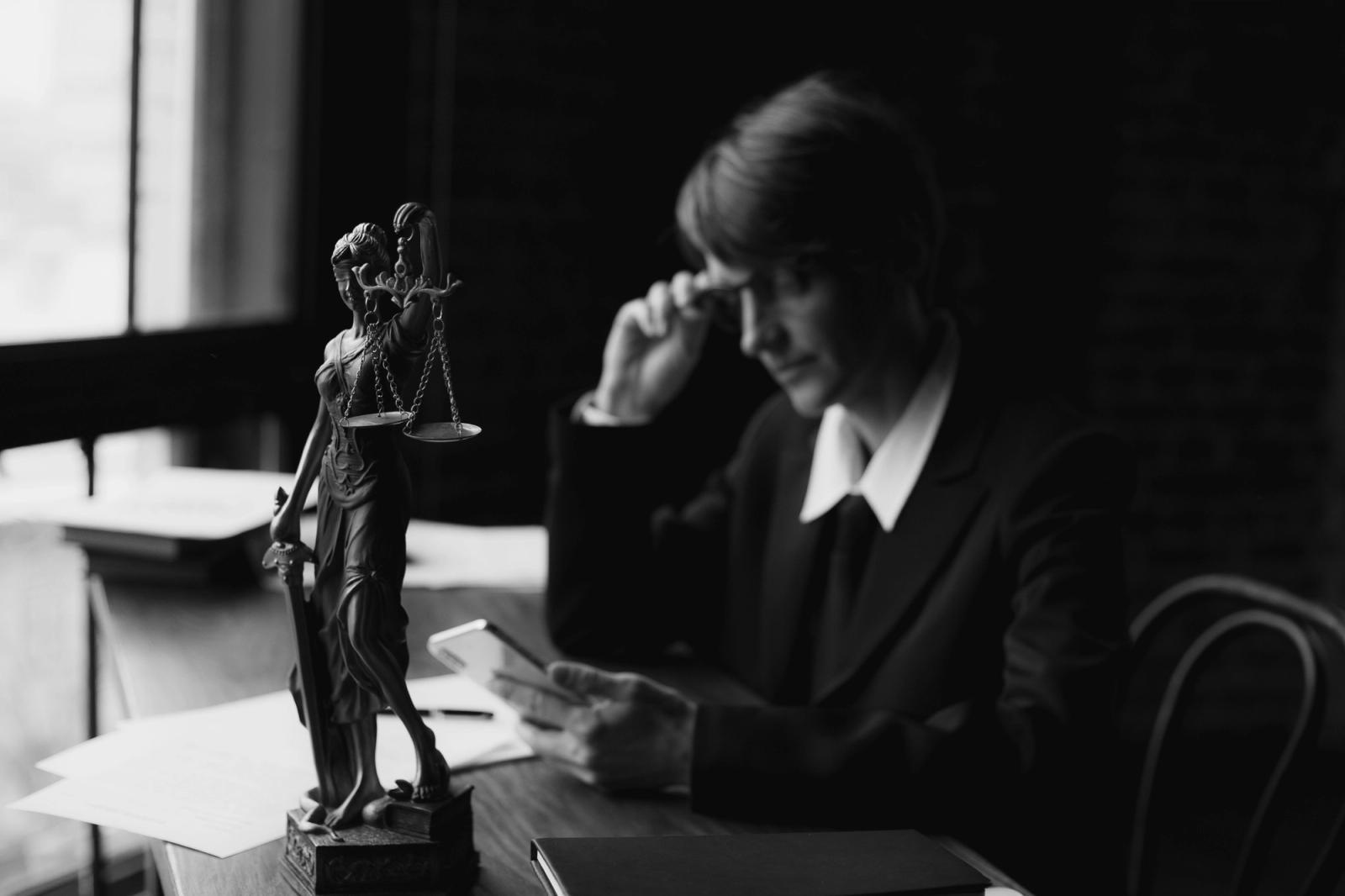 Lawyer using a mobile phone at an office desk beside a Lady Justice statue