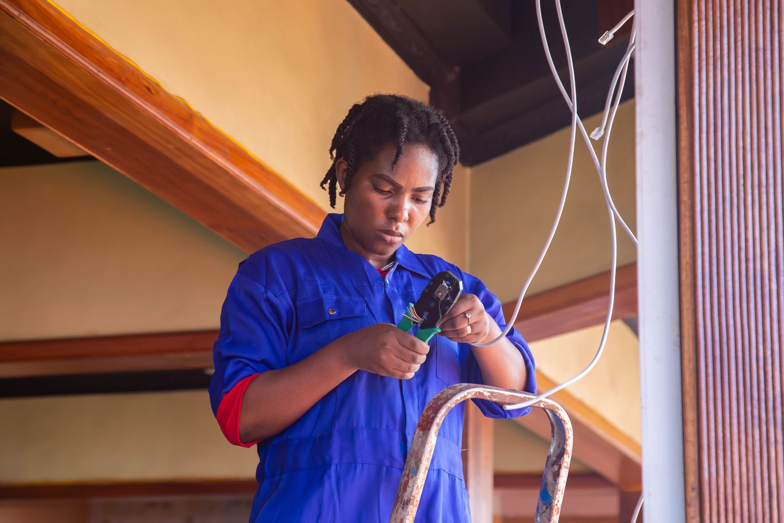 Electrician on a ladder working with electrical cables indoors