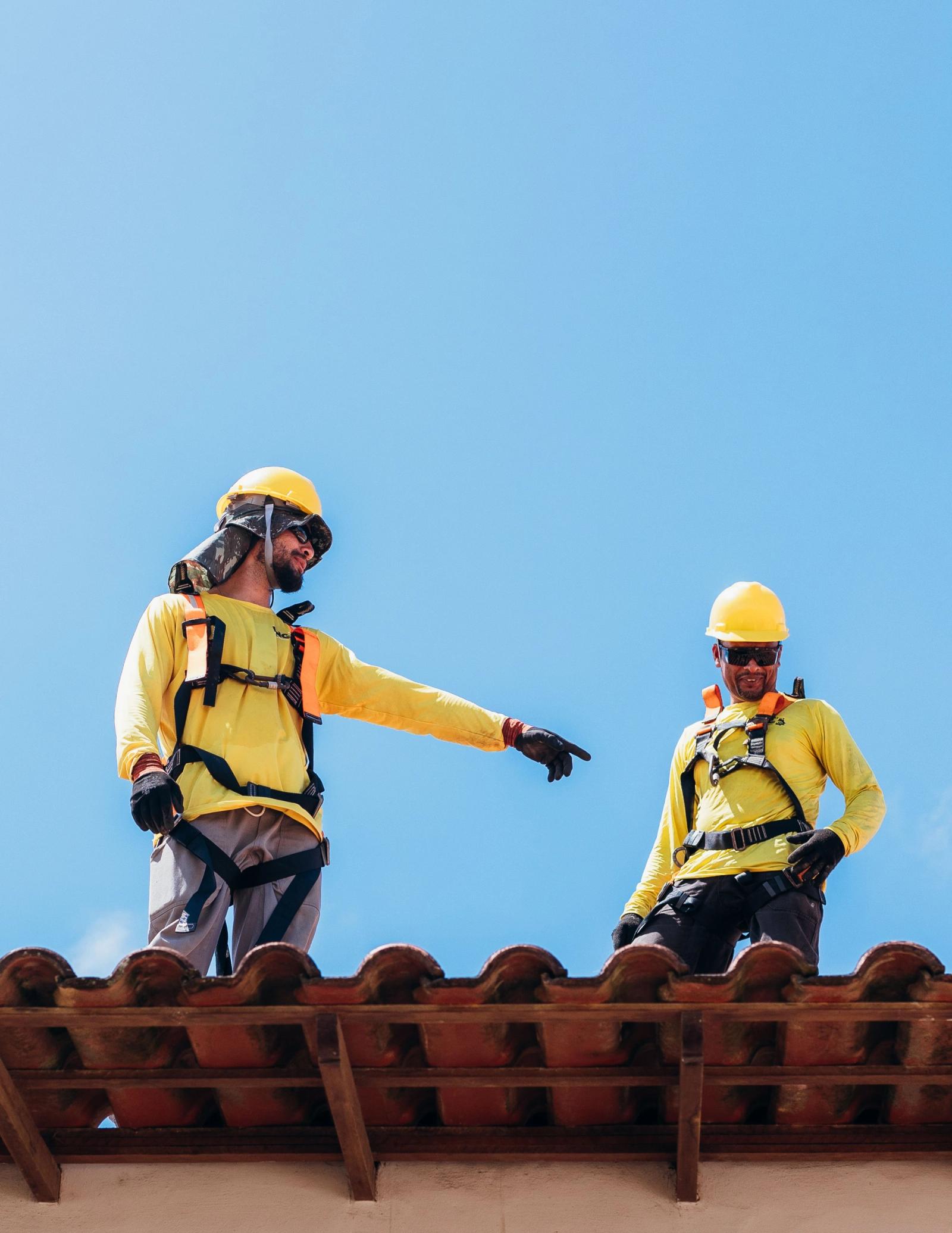 Two roofing workers in safety gear discussing work on a rooftop