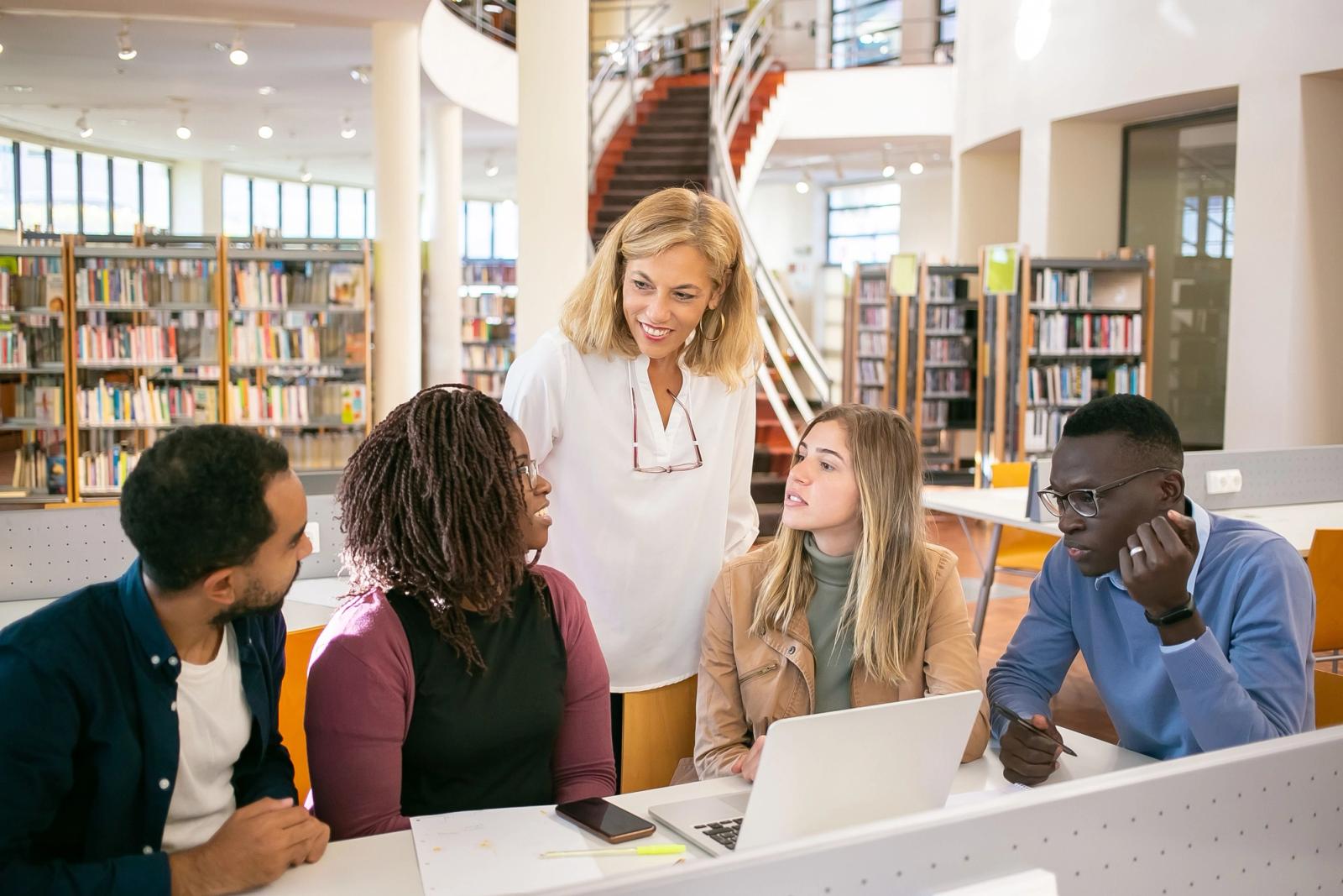University students working with an instructor around a laptop in a library