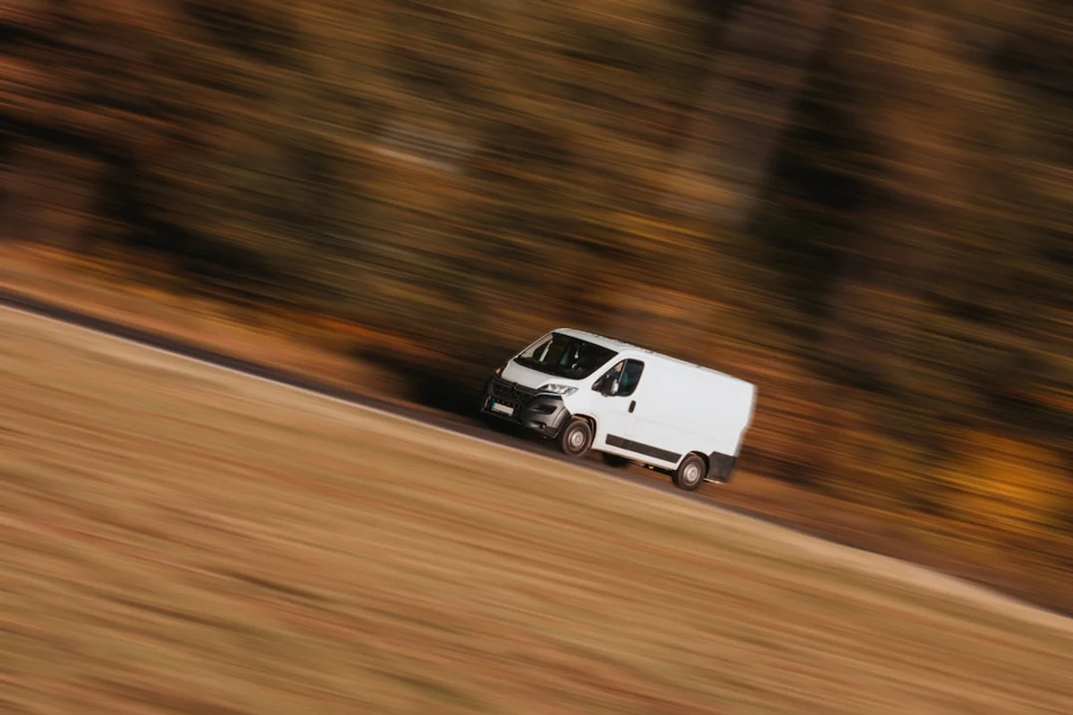 A white delivery van on a country road, caught mid-journey in a panning shot