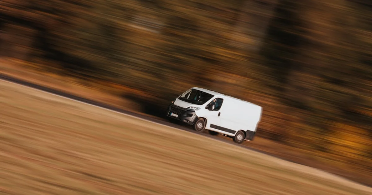 A white delivery van on a country road, caught mid-journey in a panning shot