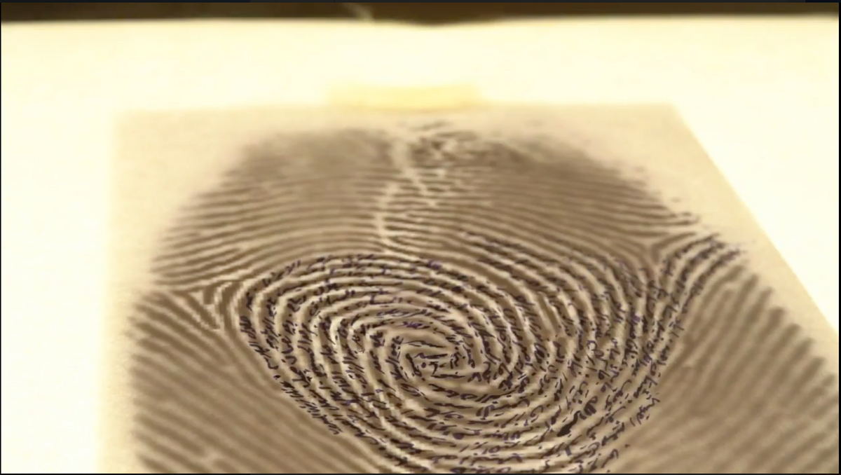 Video still from Manufactured Democracy video documentation, by Huner Emin. An off-white page on a white background is printed with an enlarged sepia colored fingerprint. In the lines of the fingerprint are handwritten names in Arabic calligraphy.