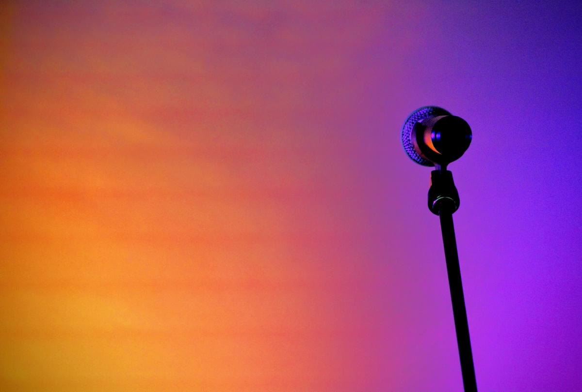 Photo of a microphone in front of an orange and purple gradient background. Photo by Joshua Hoehne on Unsplash.
