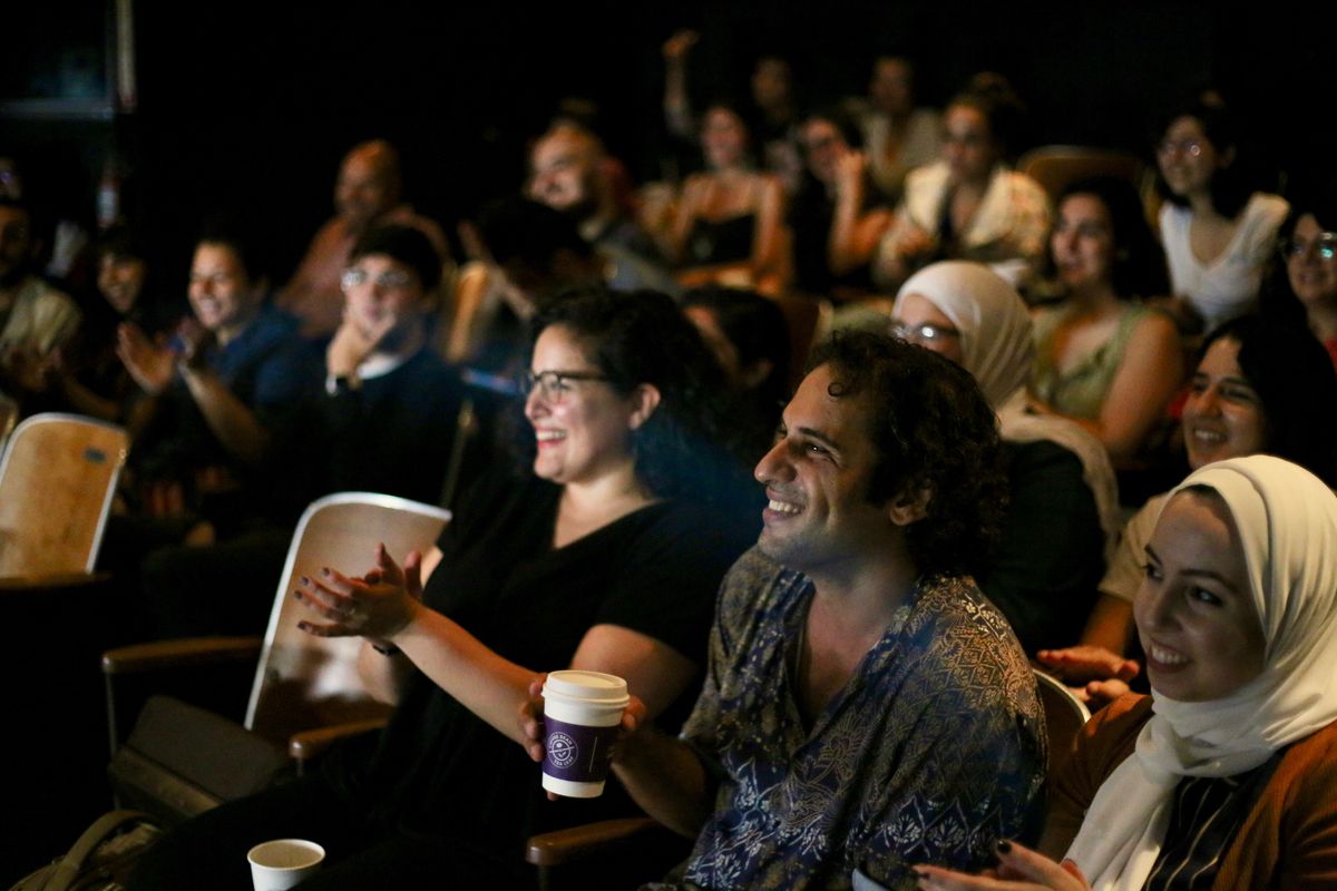 Photo by Shiyam Galyon, 2019. RAWI members sit in an auditorium clapping and smiling while watching a performance.