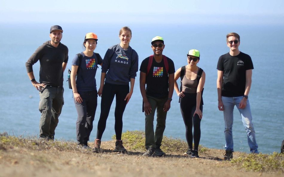 group of coworkers smiling on a dirt path in front of the ocean 