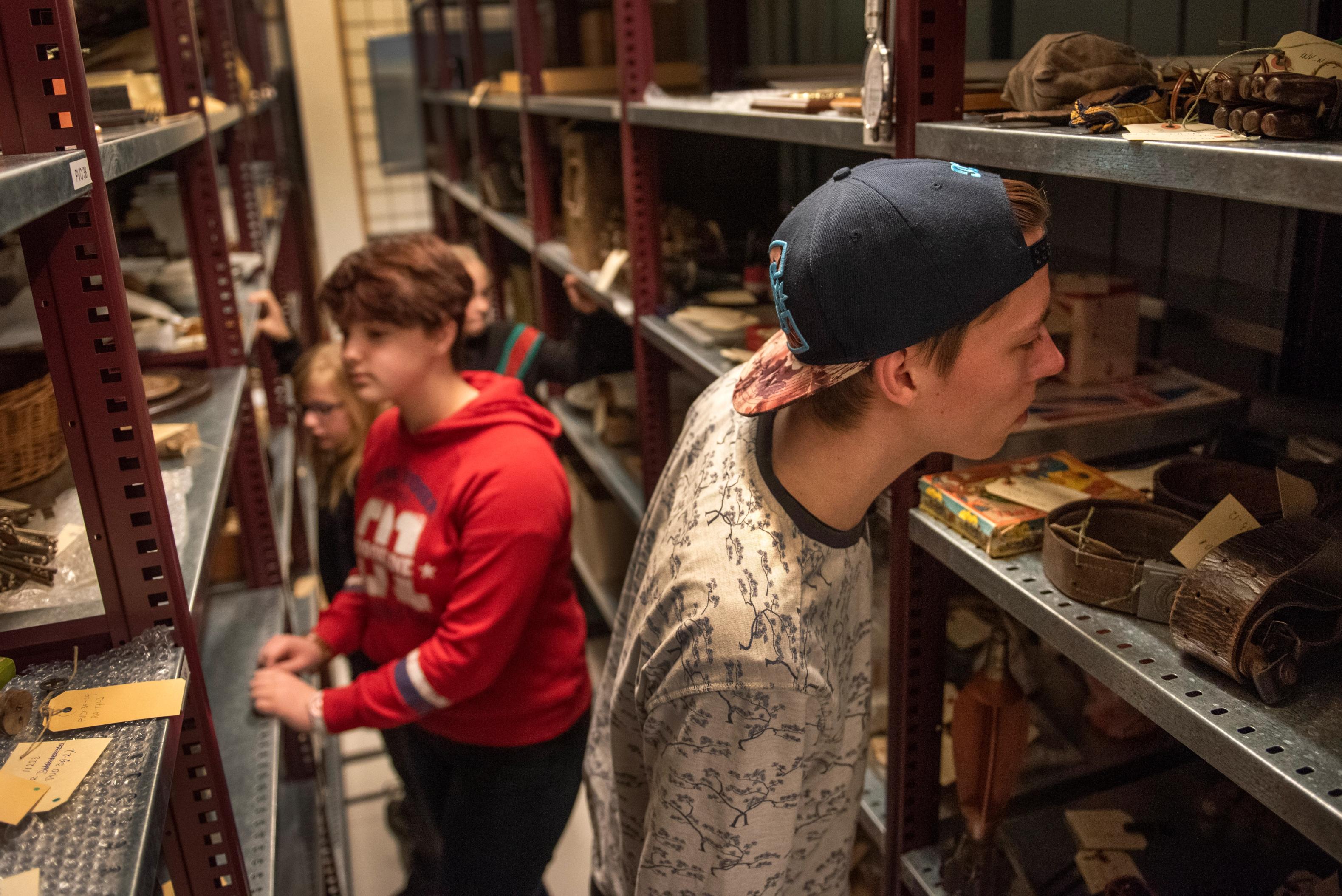 A boy in a cap and a young girl in a red jumper are looking at old artefacts fron Camp Westerbork in display cabinets