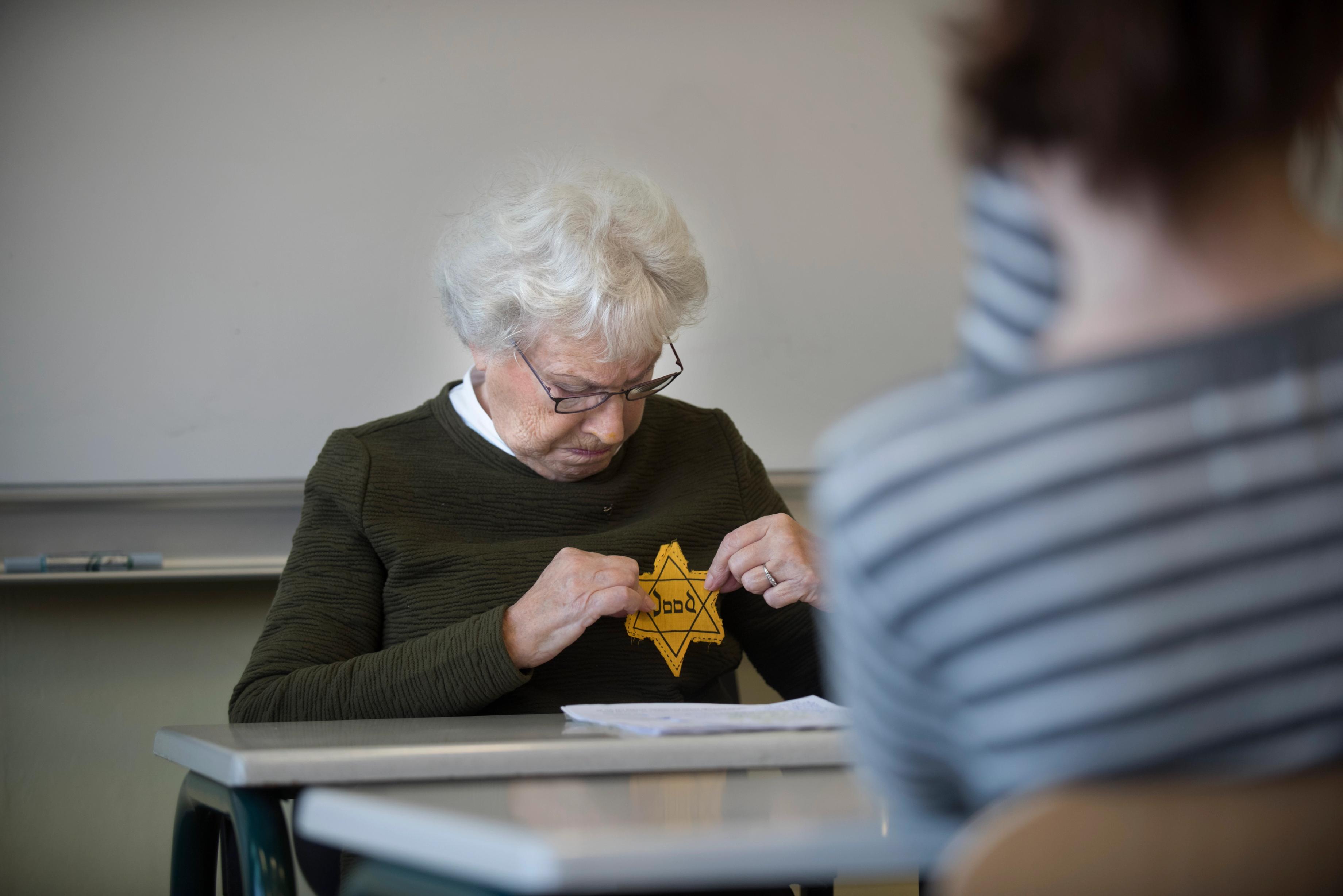 Oudere vrouw geeft gastles aan schoolklas en laat een zogeheten 'Jodenster' terwijl ze 'm omhoog houdt voor haar trui