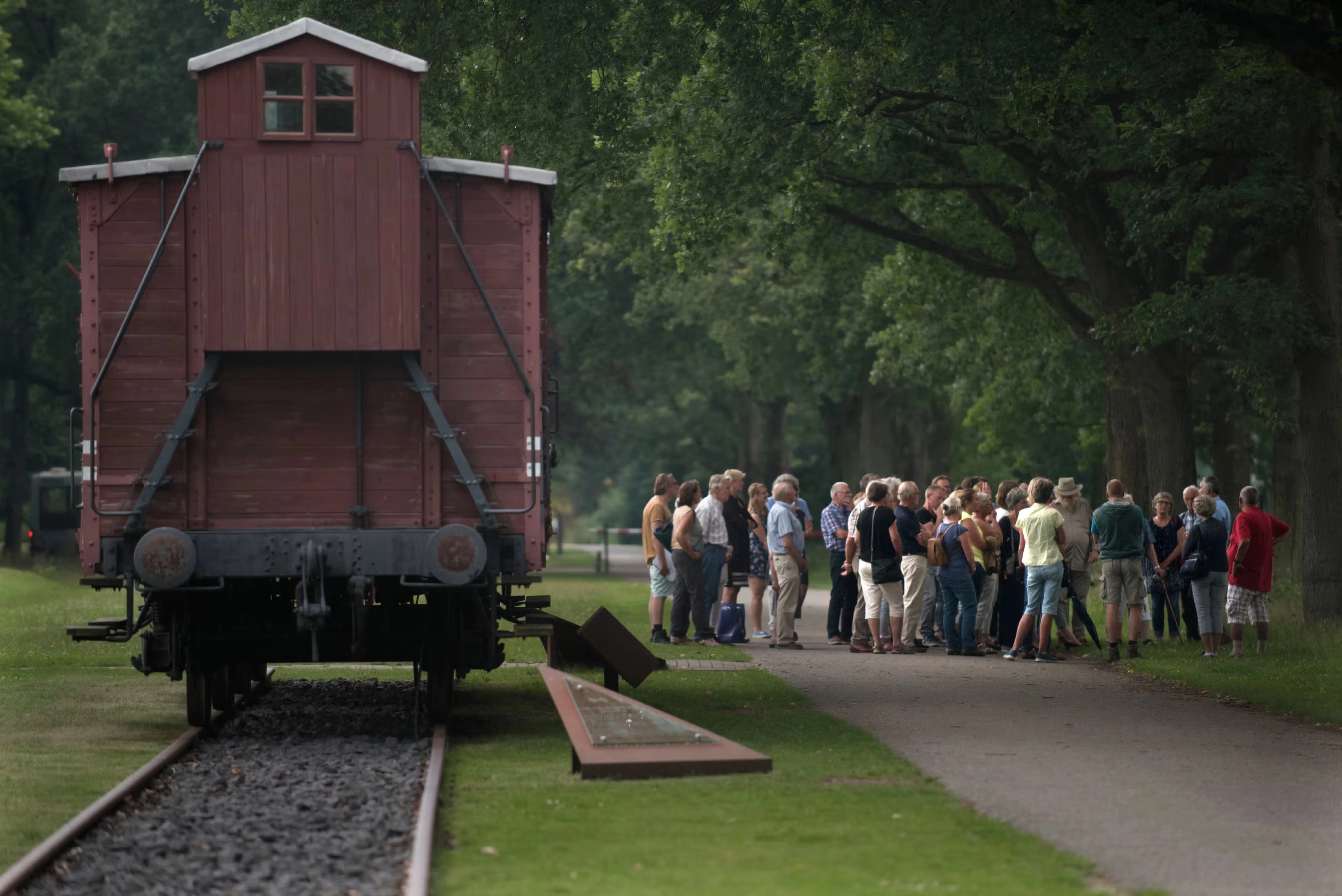 Groep mensen krijgt een rondleiding bij de wagon bij kamp westerbork