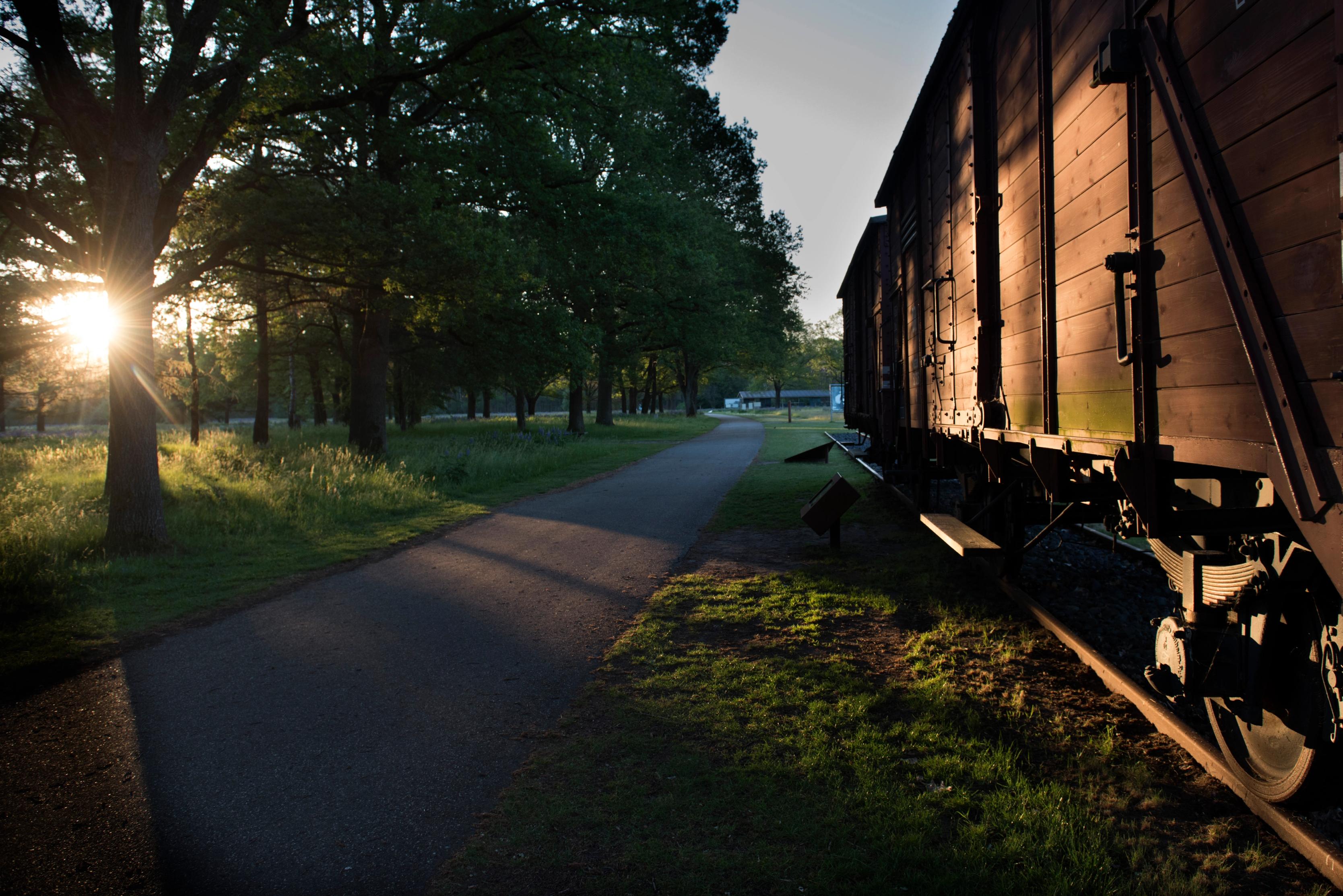 Zijkant van de wagon op het kampterrein van kamp Westerbork met een ondergaande zon achter de bomen