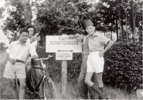 Zwart-wit collectiefoto van vier Molukse jongens die poseren bij een bord met daarop 'Kamp Schattenberg'