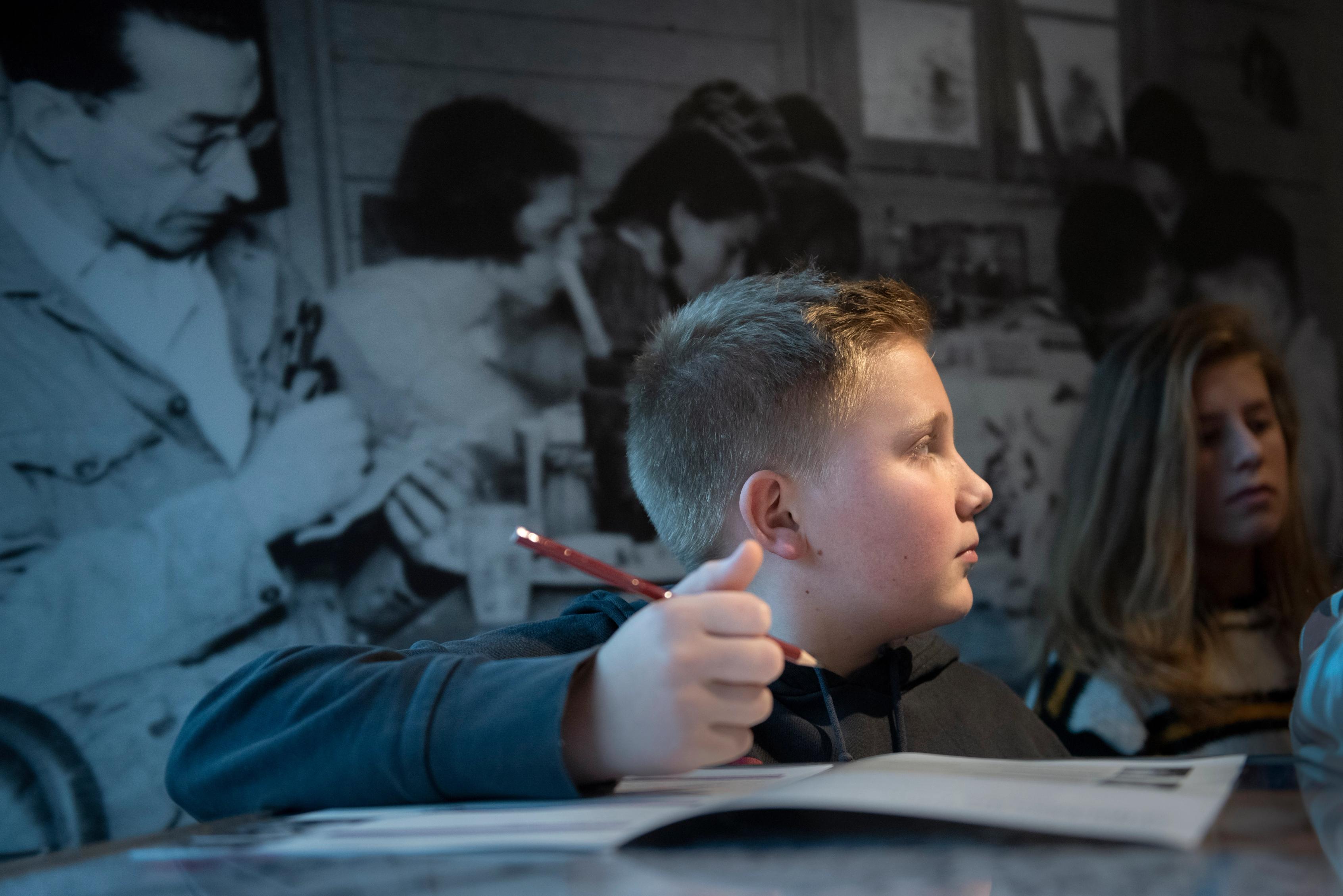 A boy is leaning on a workbook, holding a pencil, in the museum at the Camp Westerbork Memorial Centre