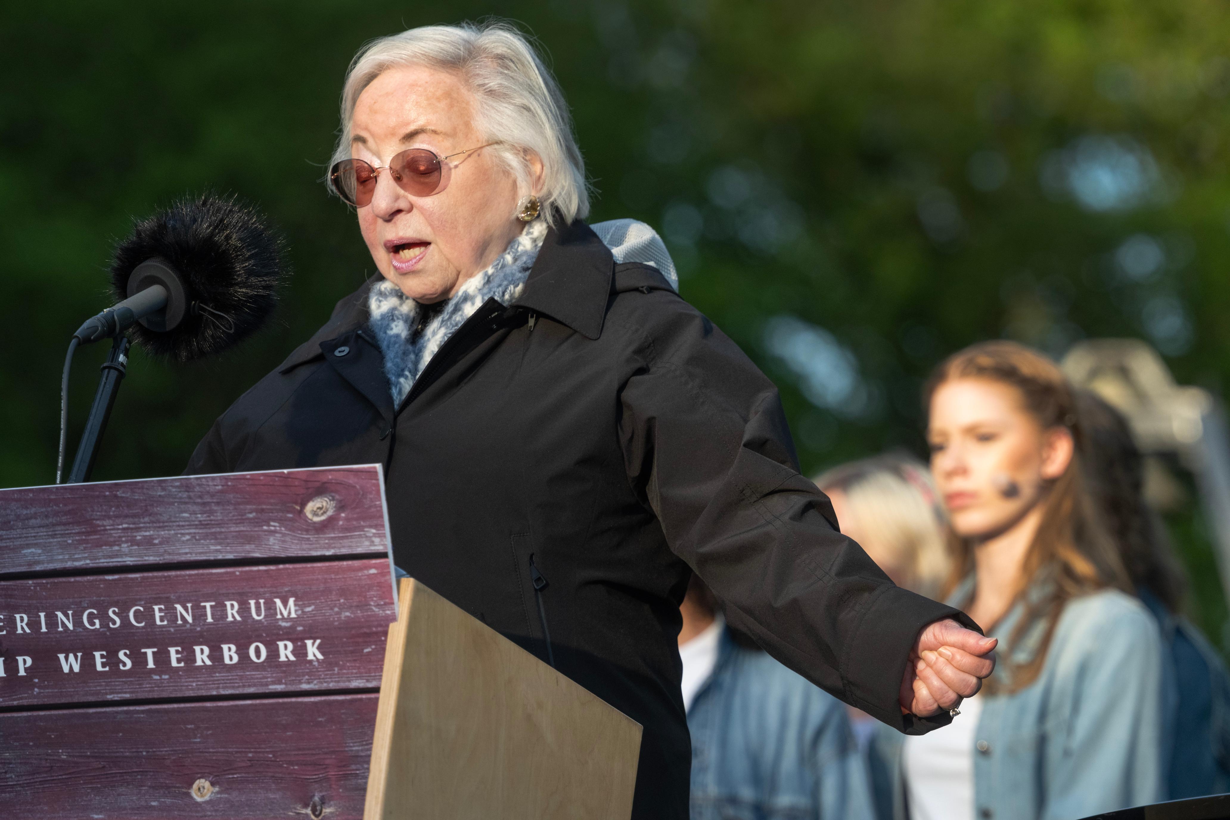 Vrouw staat achter een spreekstoel en strekt haar armen uit terwijl ze voorleest vanaf een papier tijdens de Nationale Dodenherdenking bij kamp Westerbork