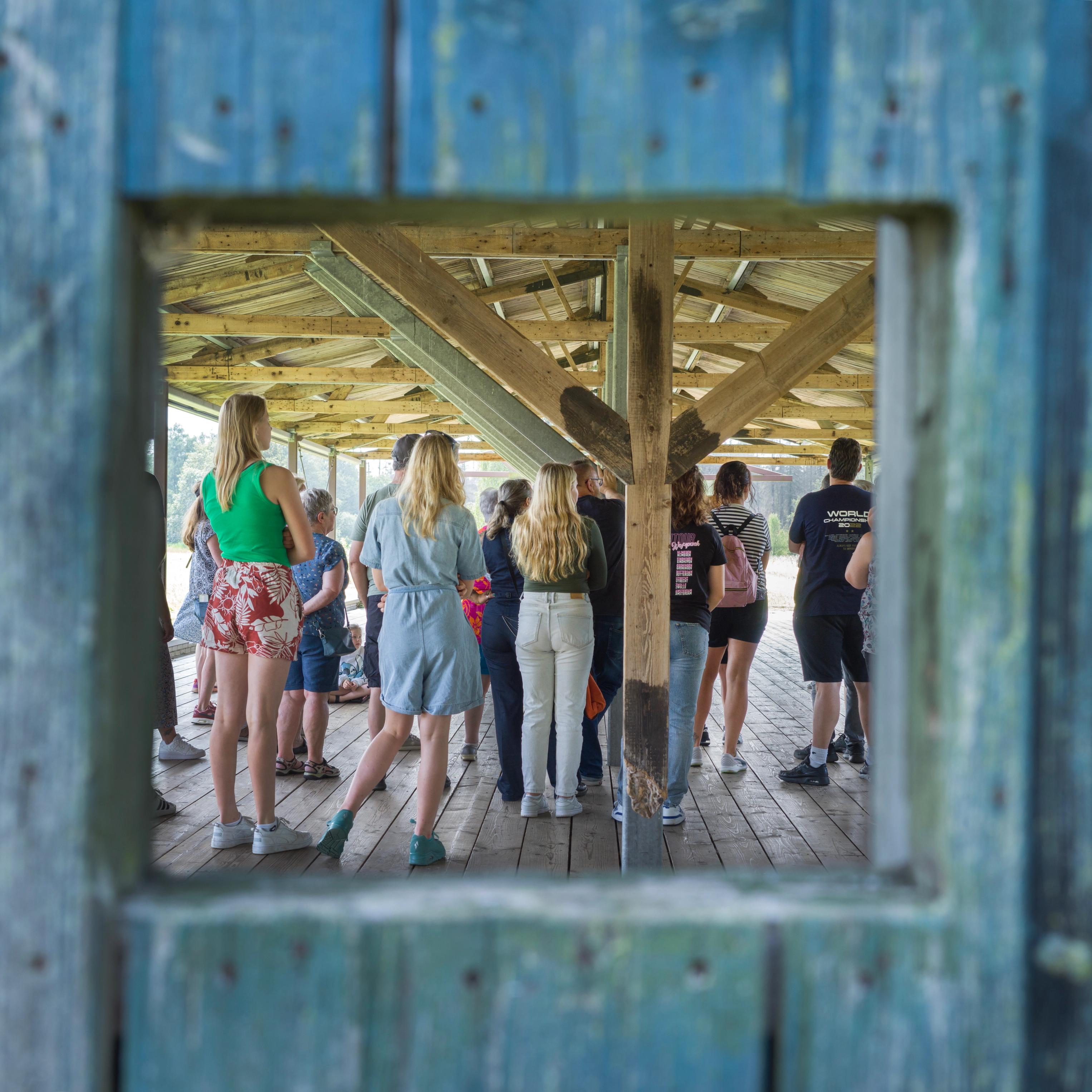A view through one of the windows in the barracks at the former Camp Westerbork, showing a group of young people taking a guided tour of the barracks