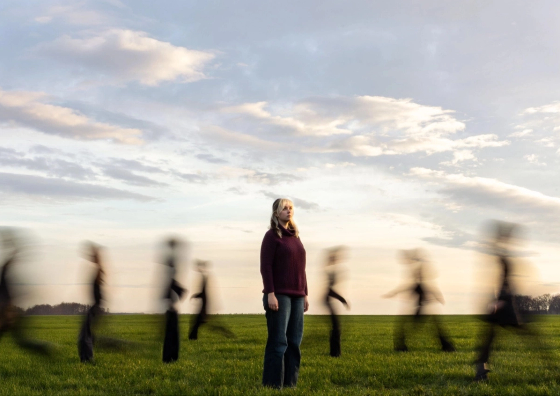 Foto van een actrice in een veld met lopende personen eromheen (uit focus)