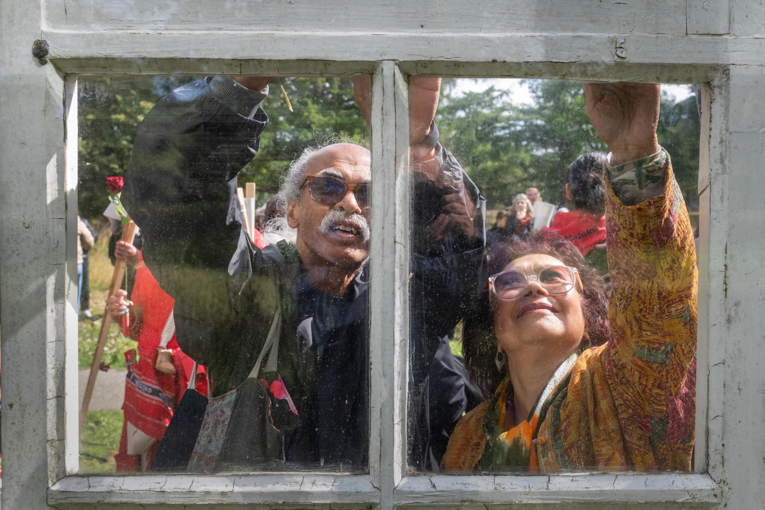 Een Molukse man en vrouw tonen eerbetoon bij het raam van het Schattenberg monument op voormalig kampterrein van kamp Westerbork