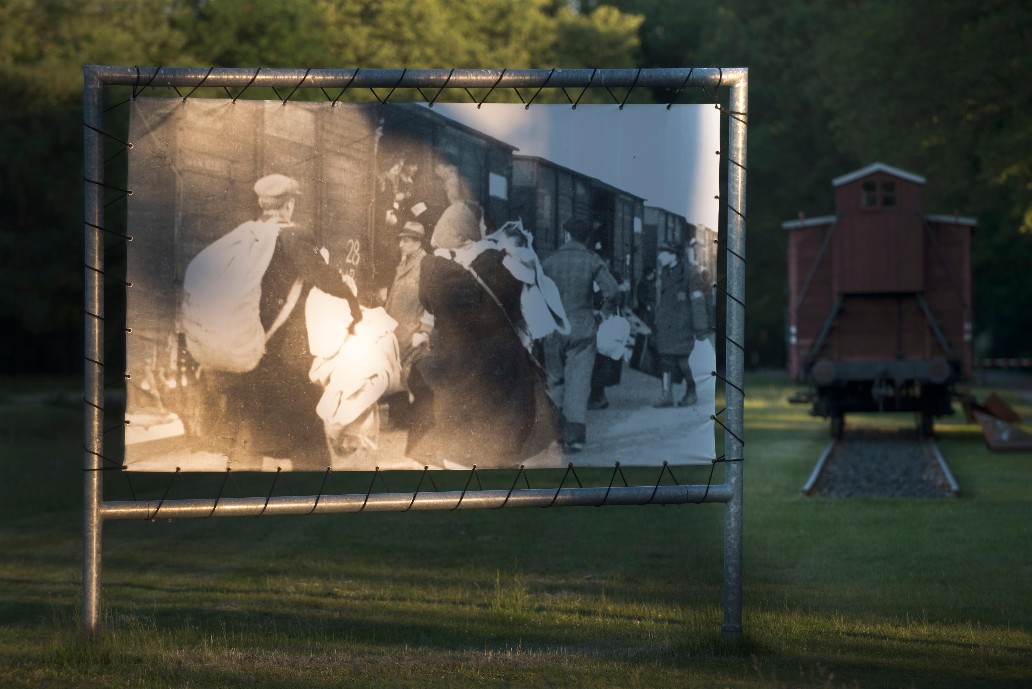 Uitvergrote foto op het voormalig kampterrein van kamp Westerbork. Op het paneel is een zwart-wit foto te zien van kampgevangenen die naar de trein wandelen voor transport
