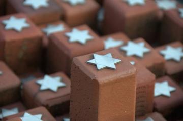 Close-up van een paar stenen in het 102.000 Stenen Monument bij kamp Westerbork. Bovenop de terracotta stenen zijn zilveren Jodensterren te zien