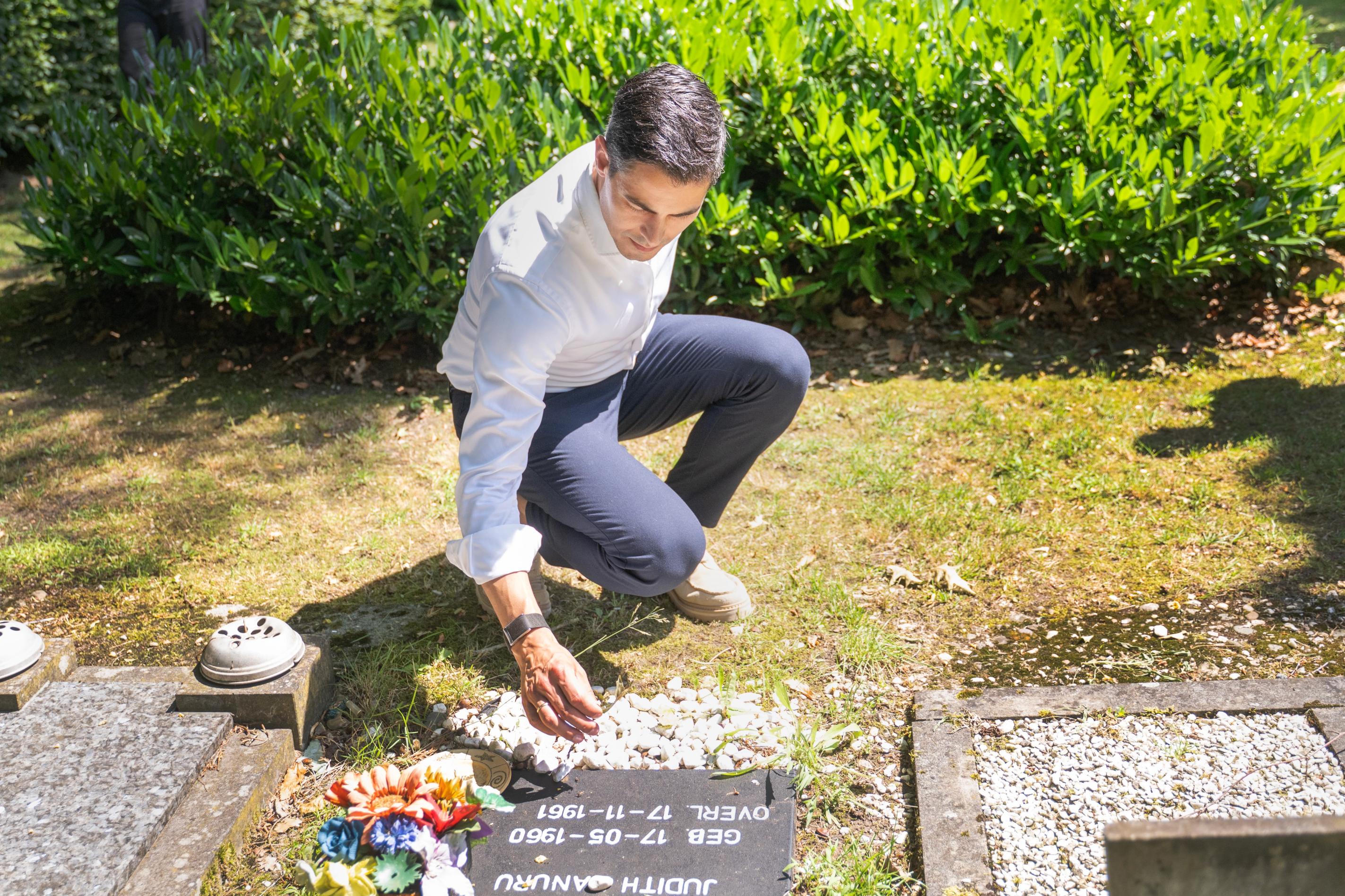 Minister-president Rob Jetten bukt bij een grafsteen en haalt een takje weg