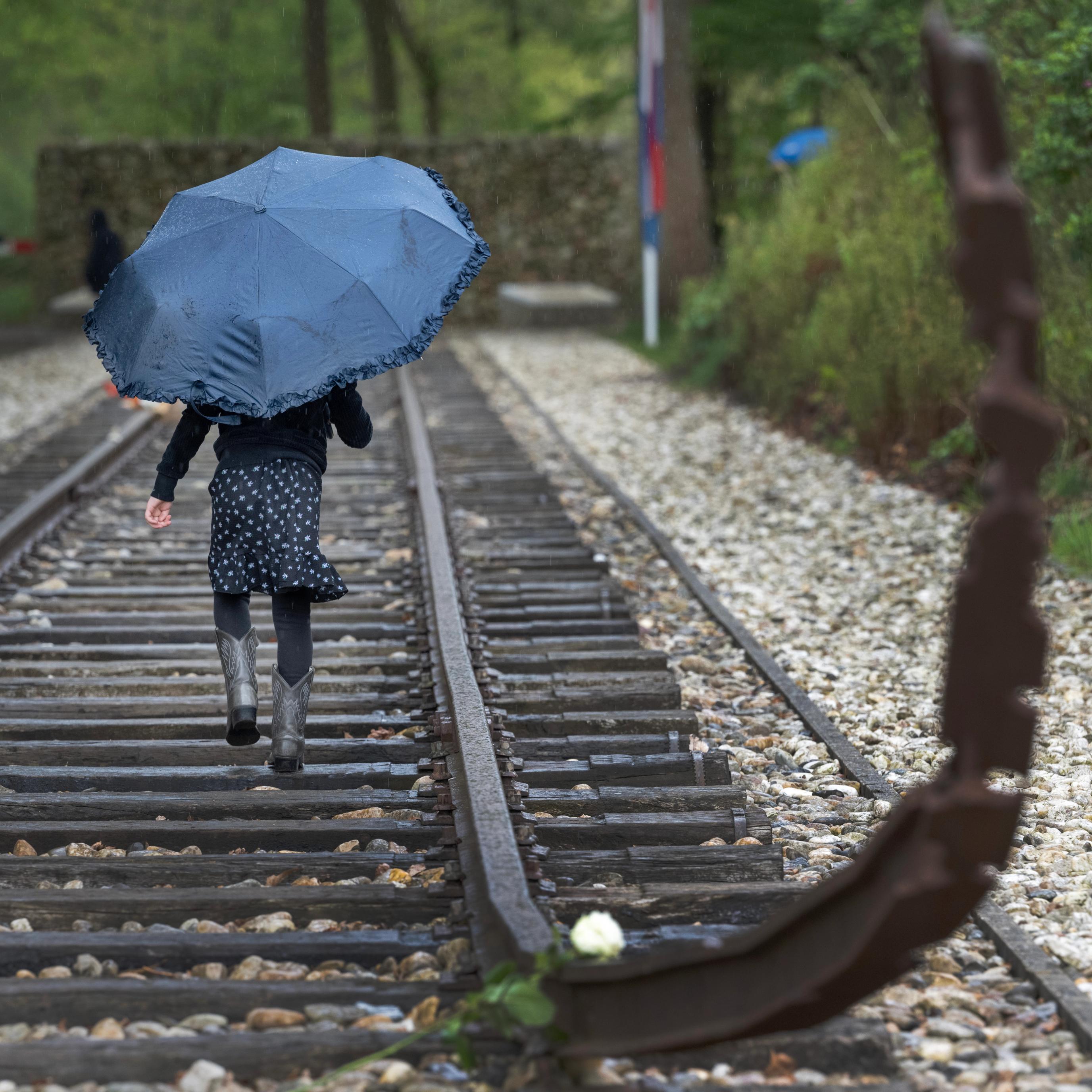 A young girl is running along the railway tracks with a blue umbrella