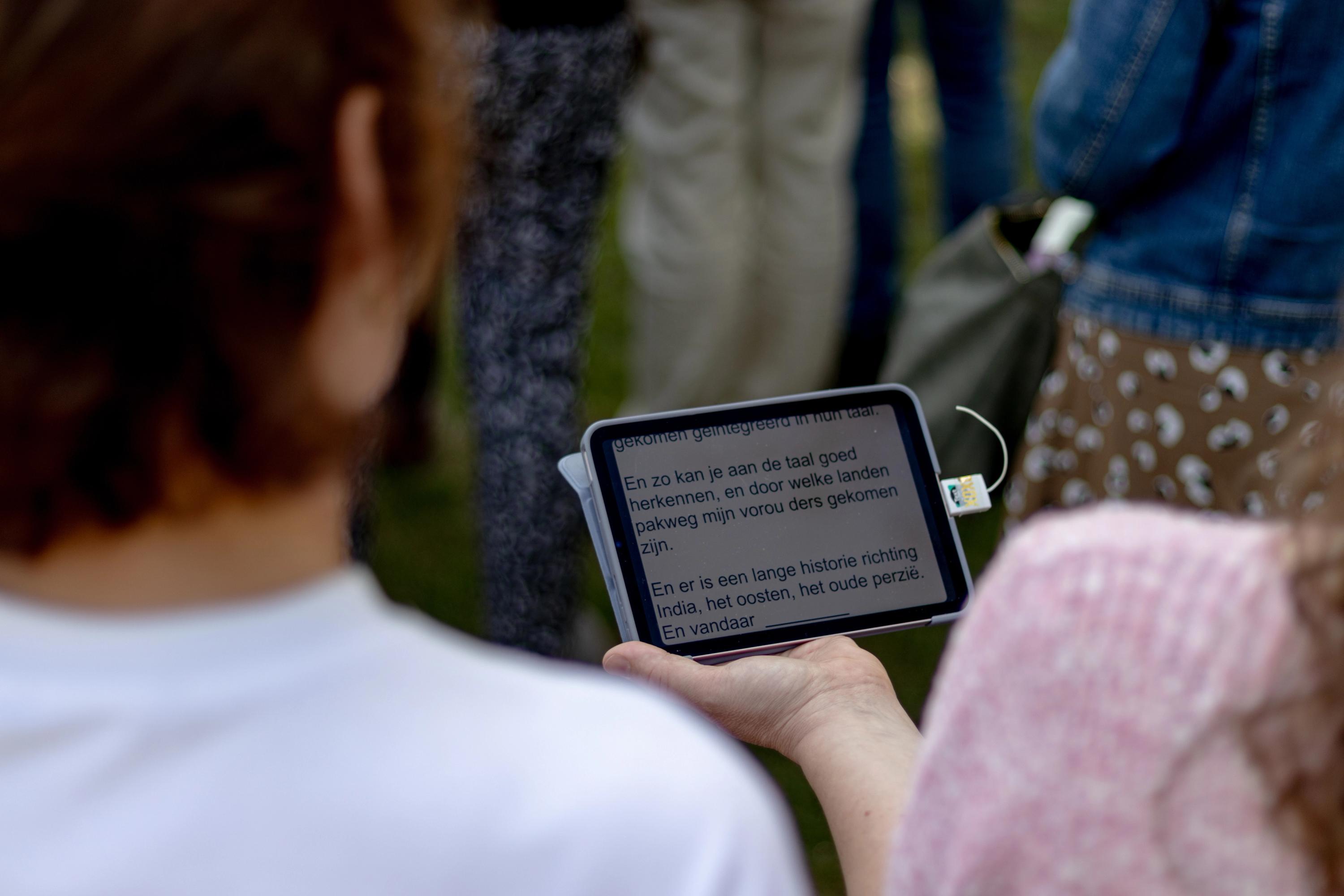 A woman is holding a tablet displaying text written by a text interpreter (Velowalker) during a guided tour of Camp Westerbork