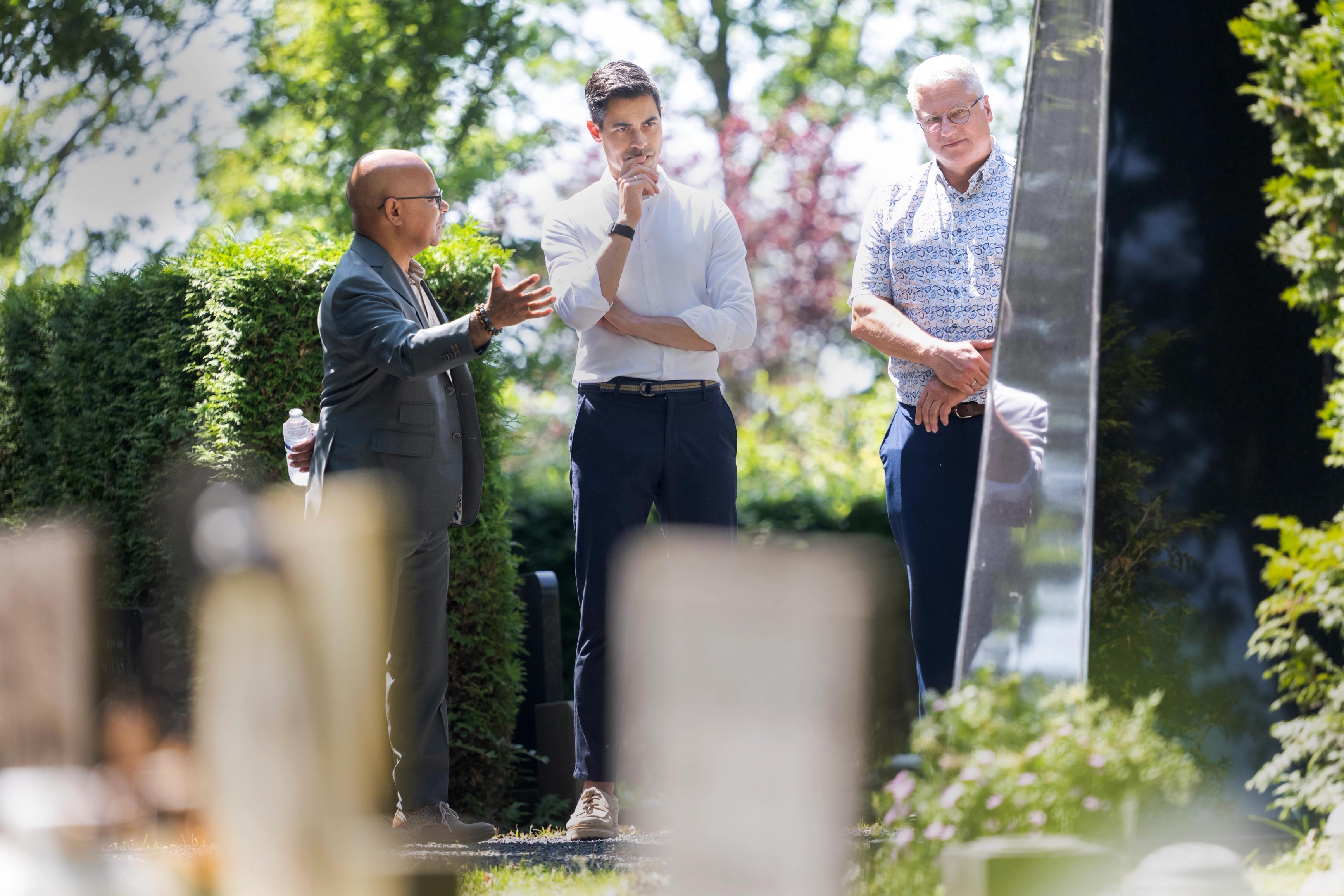 Minister-president Rob Jetten bekijk monument op begraafplaats terwijl John Matahelumual uitleg geeft en burgemeester Jan Zwiers meekijkt