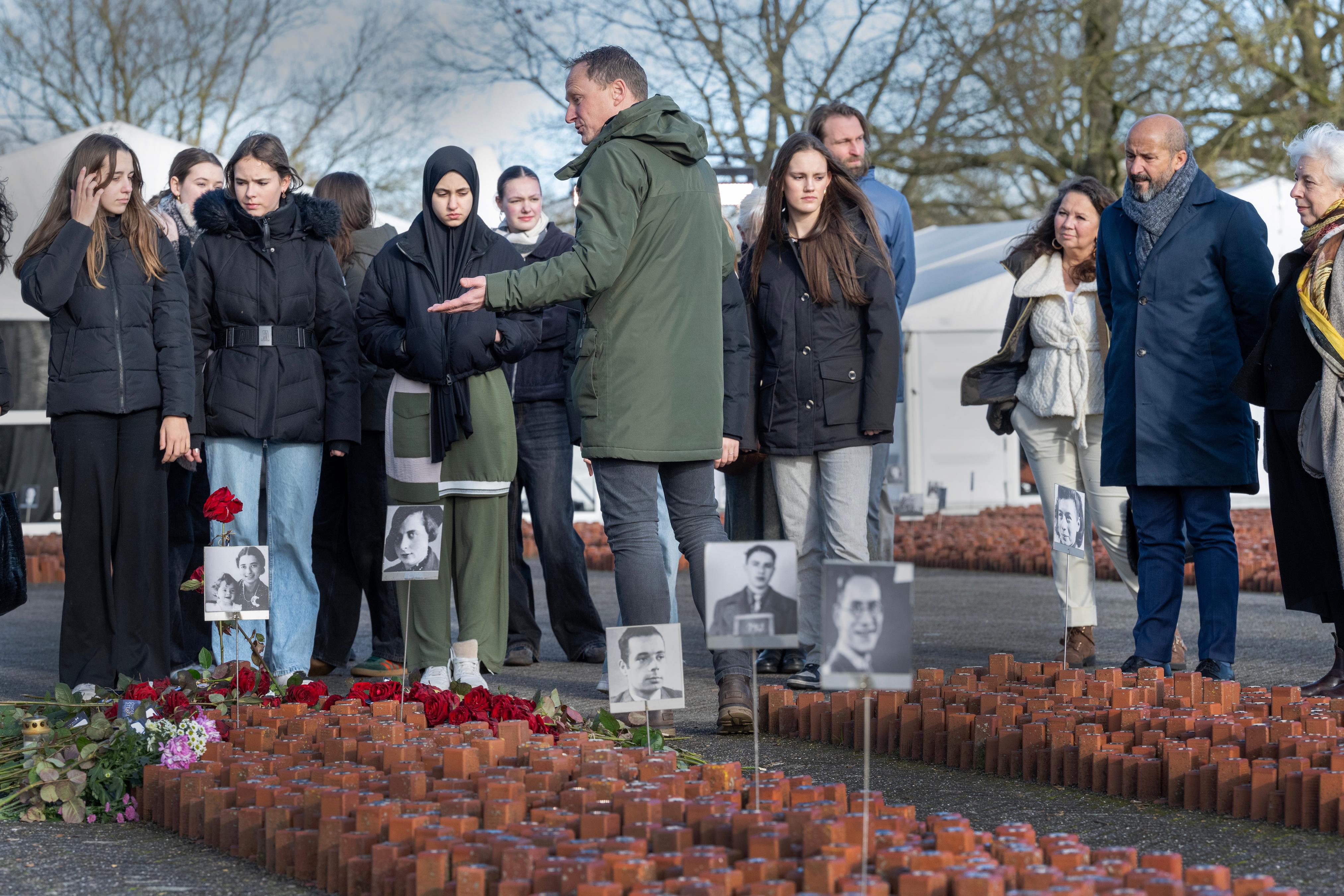 Groep mensen kijkt naar man die rondleiding geeft bij het 102.000 stenen monument van kamp westerbork