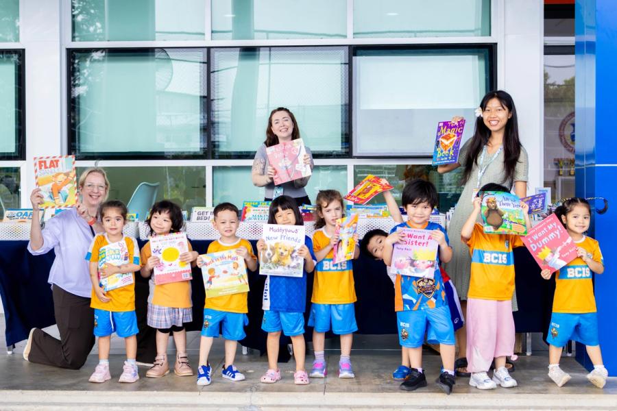 A group of young BCIS pupils stand with two members of staff, each holding up a book from the fair.