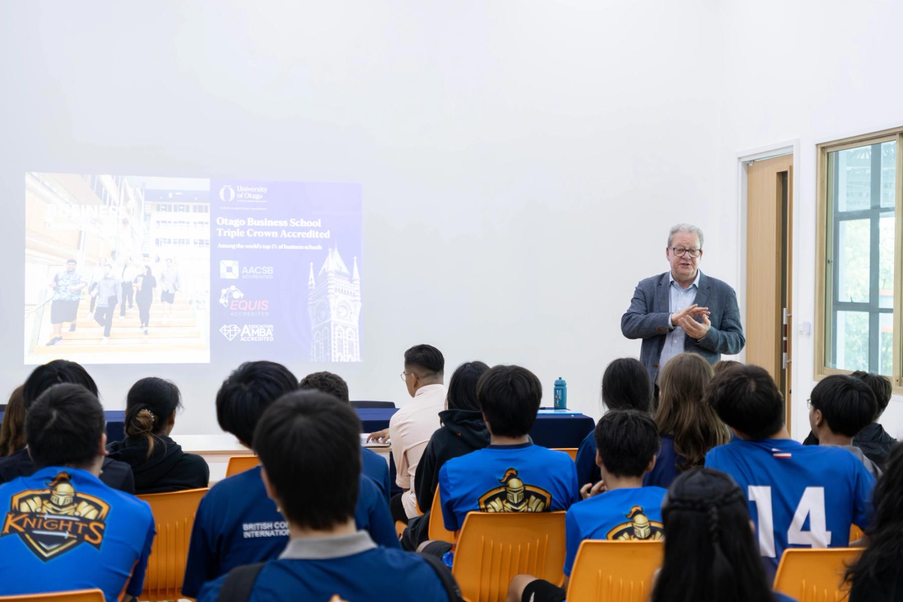 Year 10 and 11 BCIS students, some in Knights sports kit, listen to Mr Garry Chronican present a slide on Otago Business School's accreditation from AACSB, EQUIS and AMBA.