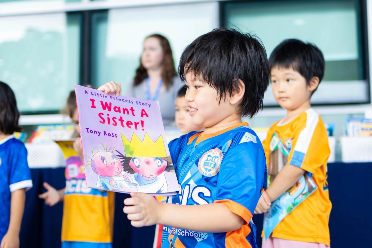 A young BCIS pupil holds up his choice, A Little Princess Story: I Want a Sister! by Tony Ross, at the book fair.