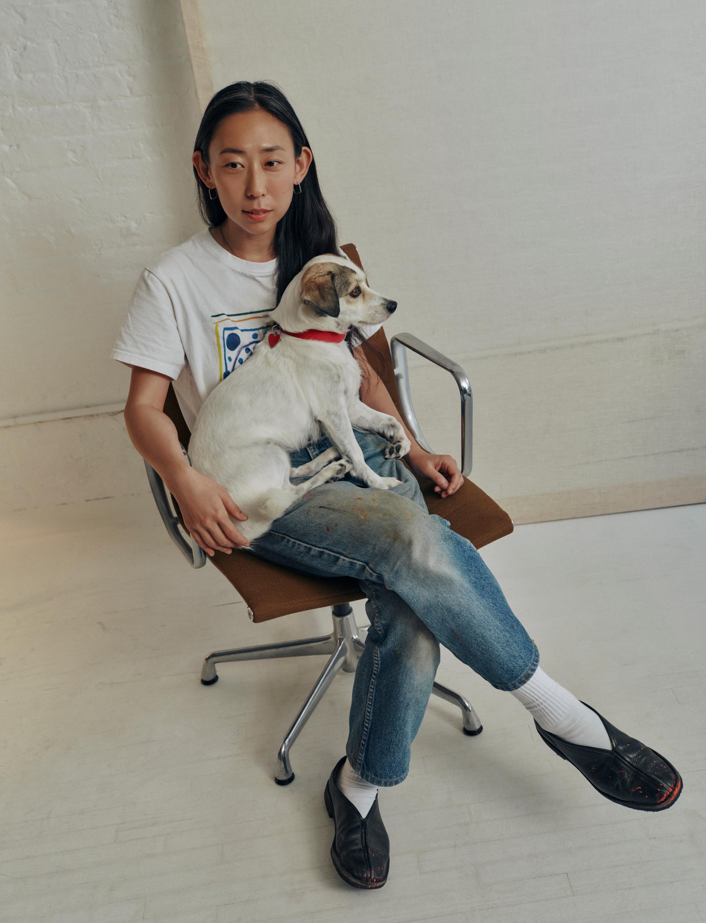 Artist Na Kim is sitting on a chair with her dog.
