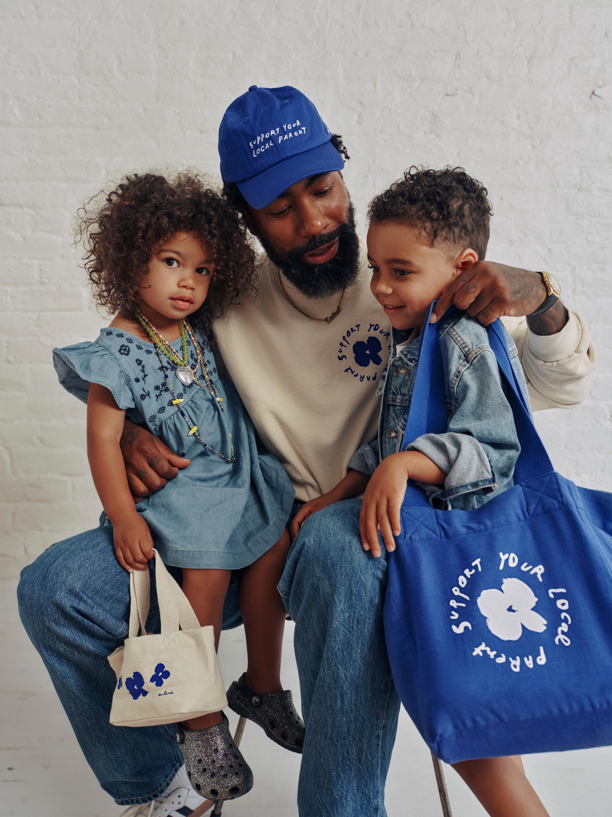 A man is seen wearing the SYLP crewneck and hat, while his kids sport the canvas tote and mini tote.