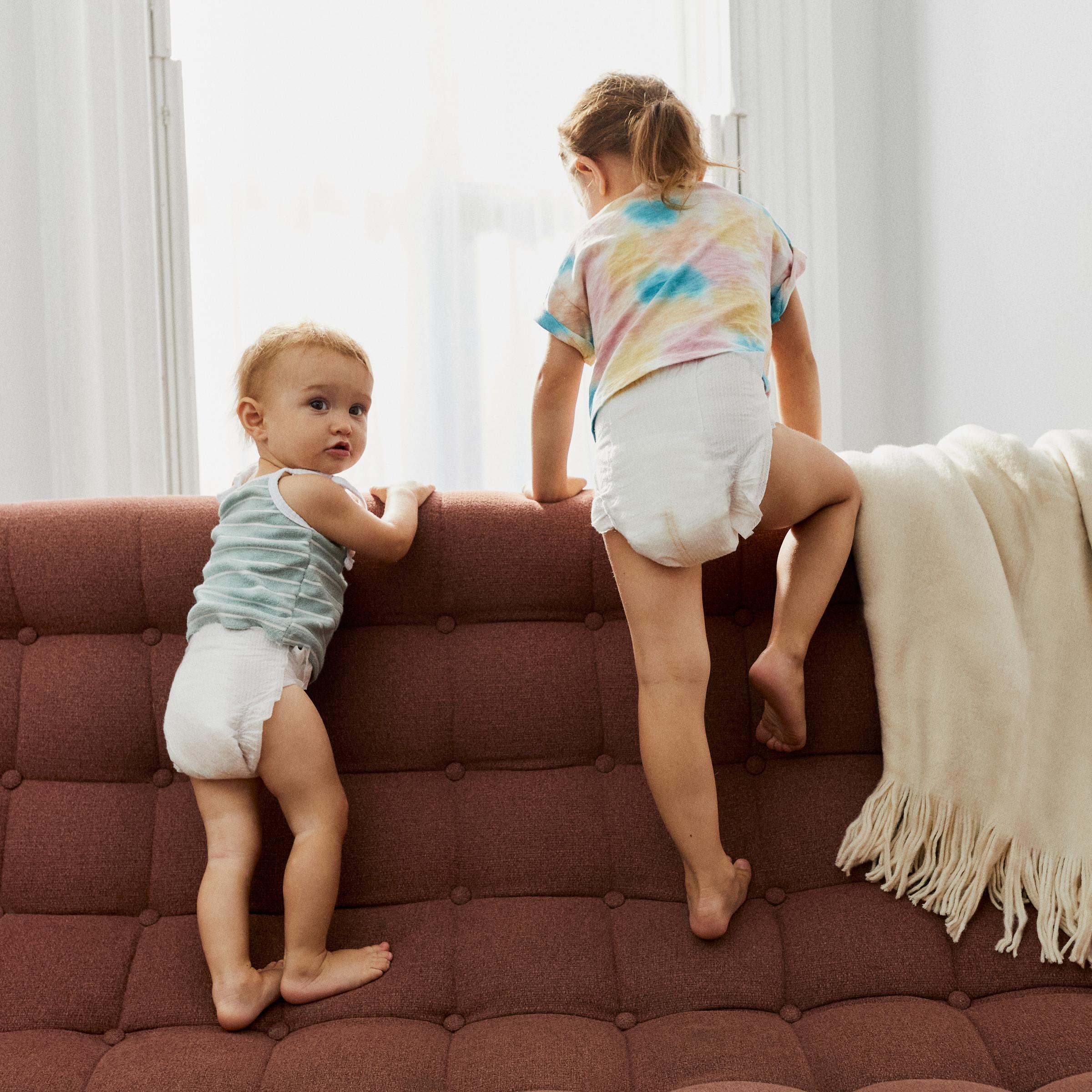 two children are climbing on the base of a couch.