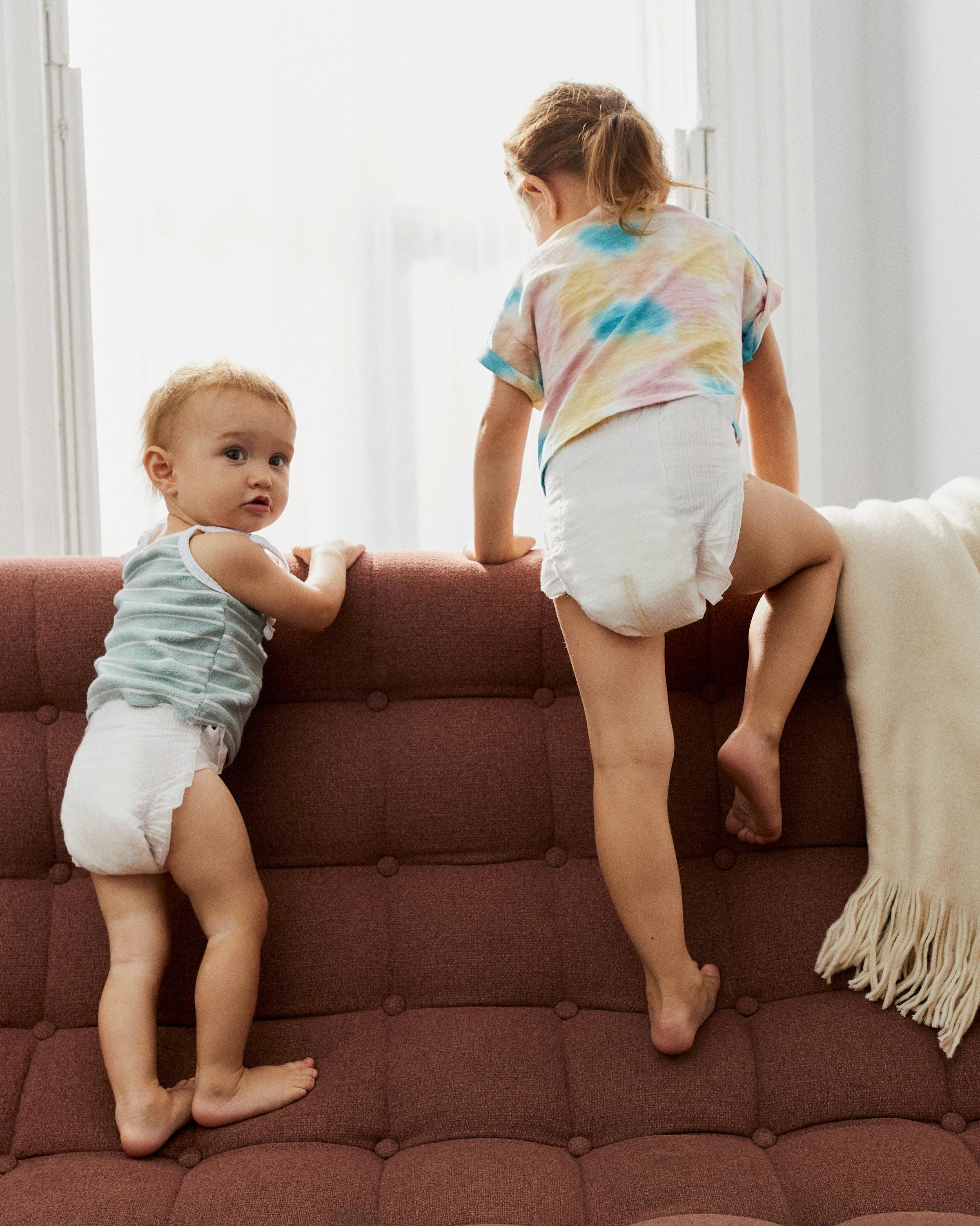 two children are climbing on the base of a couch.