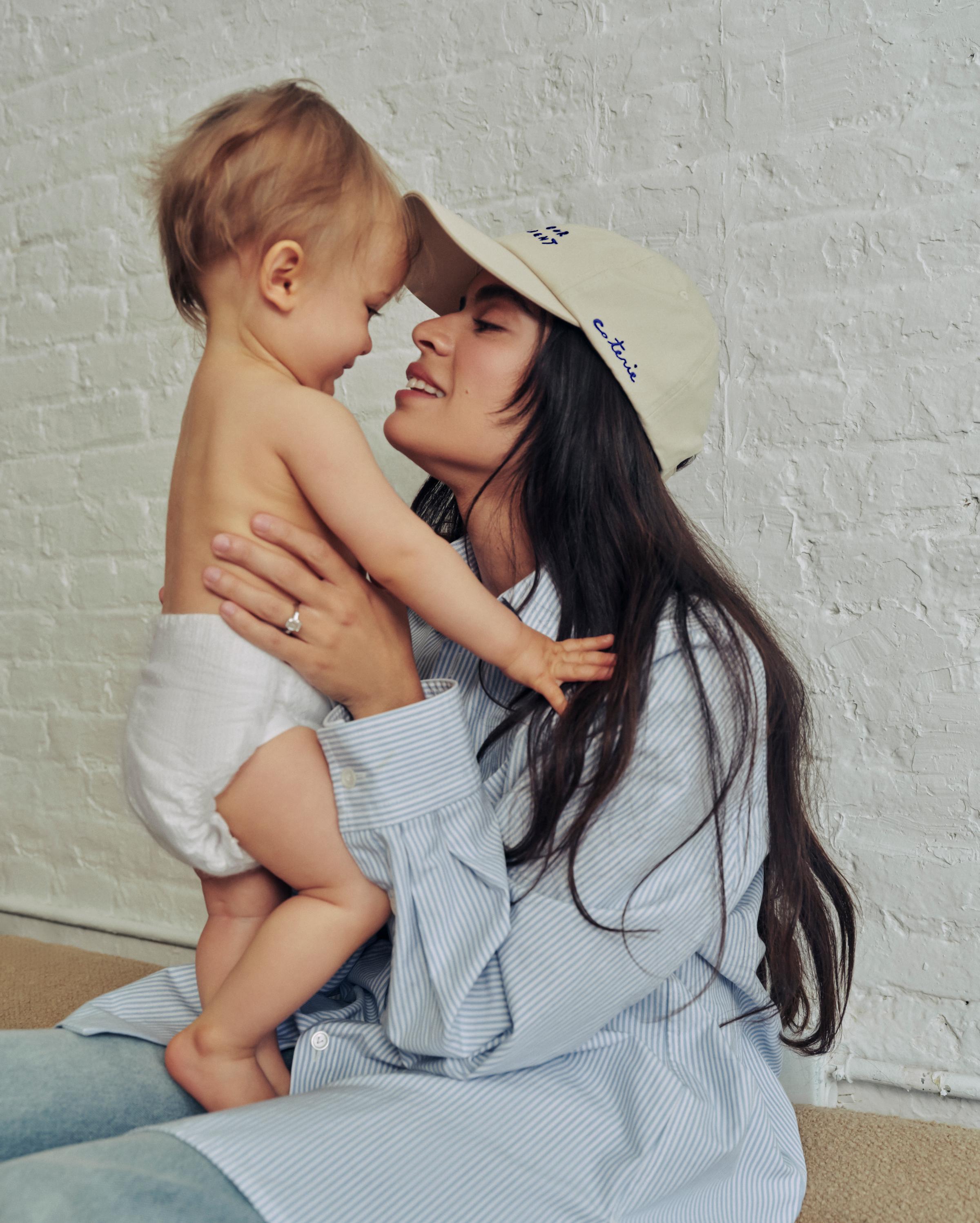 A woman, wearing a SYLP classic cap, is holding her toddler.