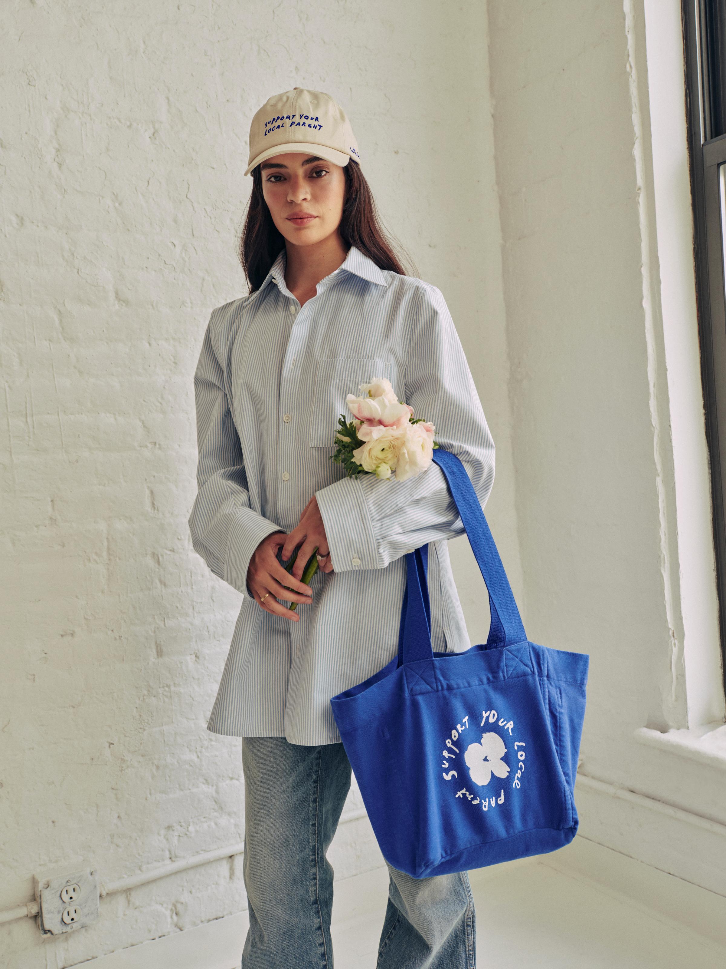 A woman is carrying the SYLP electric blue canvas tote in one arm.