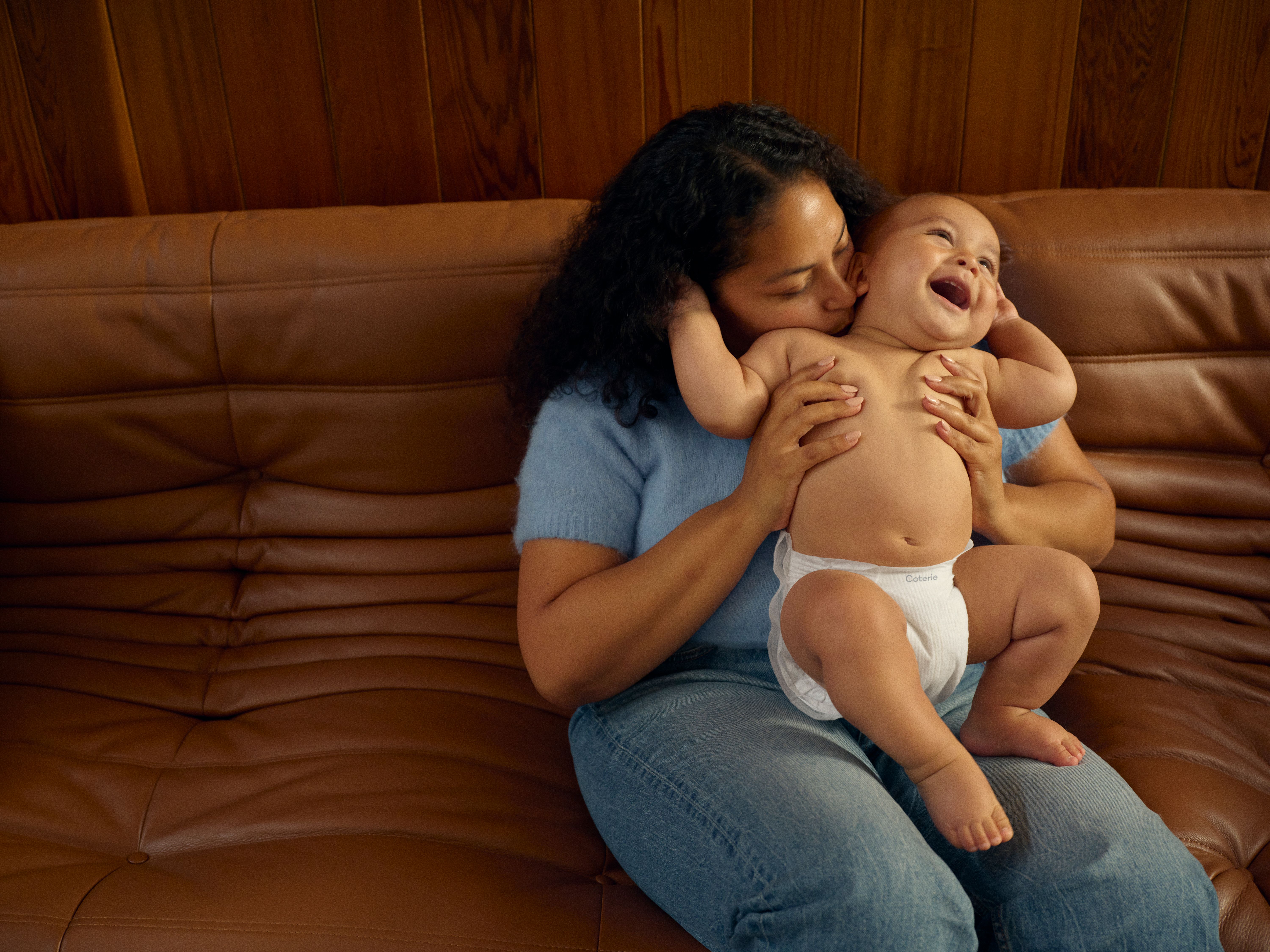 a baby stands up on a couch with the support of his mother and father.