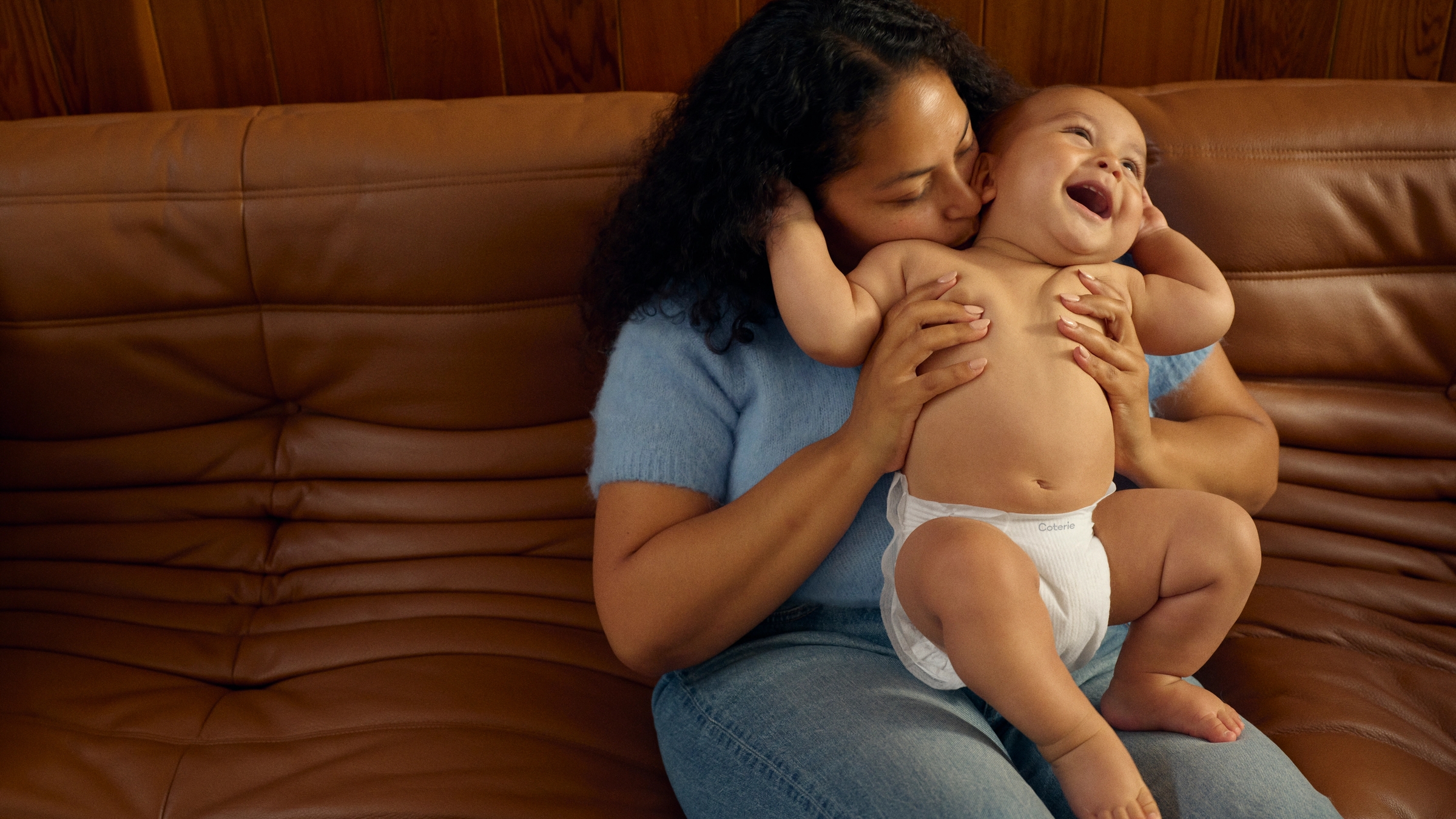 a baby stands up on a couch with the support of his mother and father.