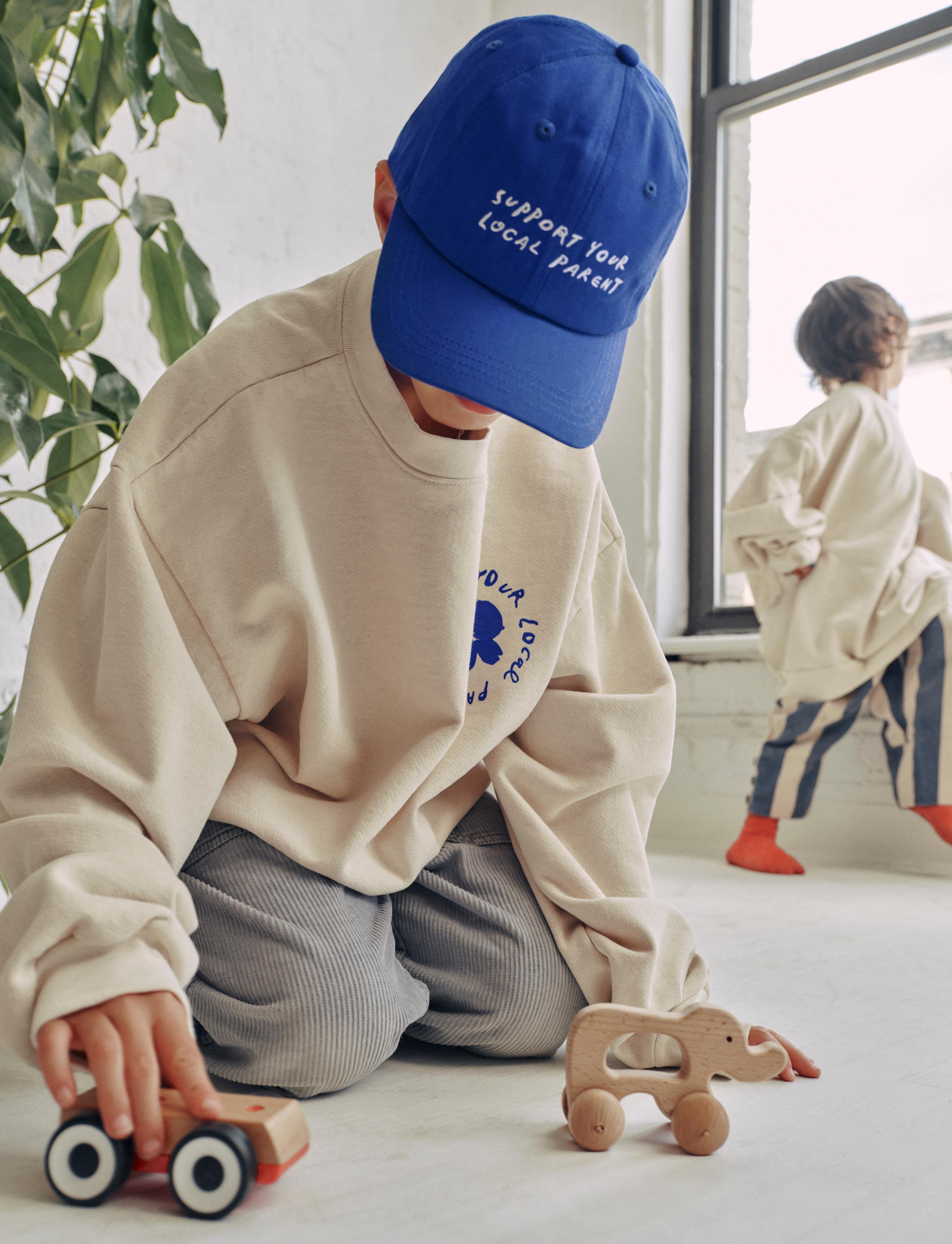 A little boy sits on the floor playing with wooden figurines in an electric blue SYLP hat.